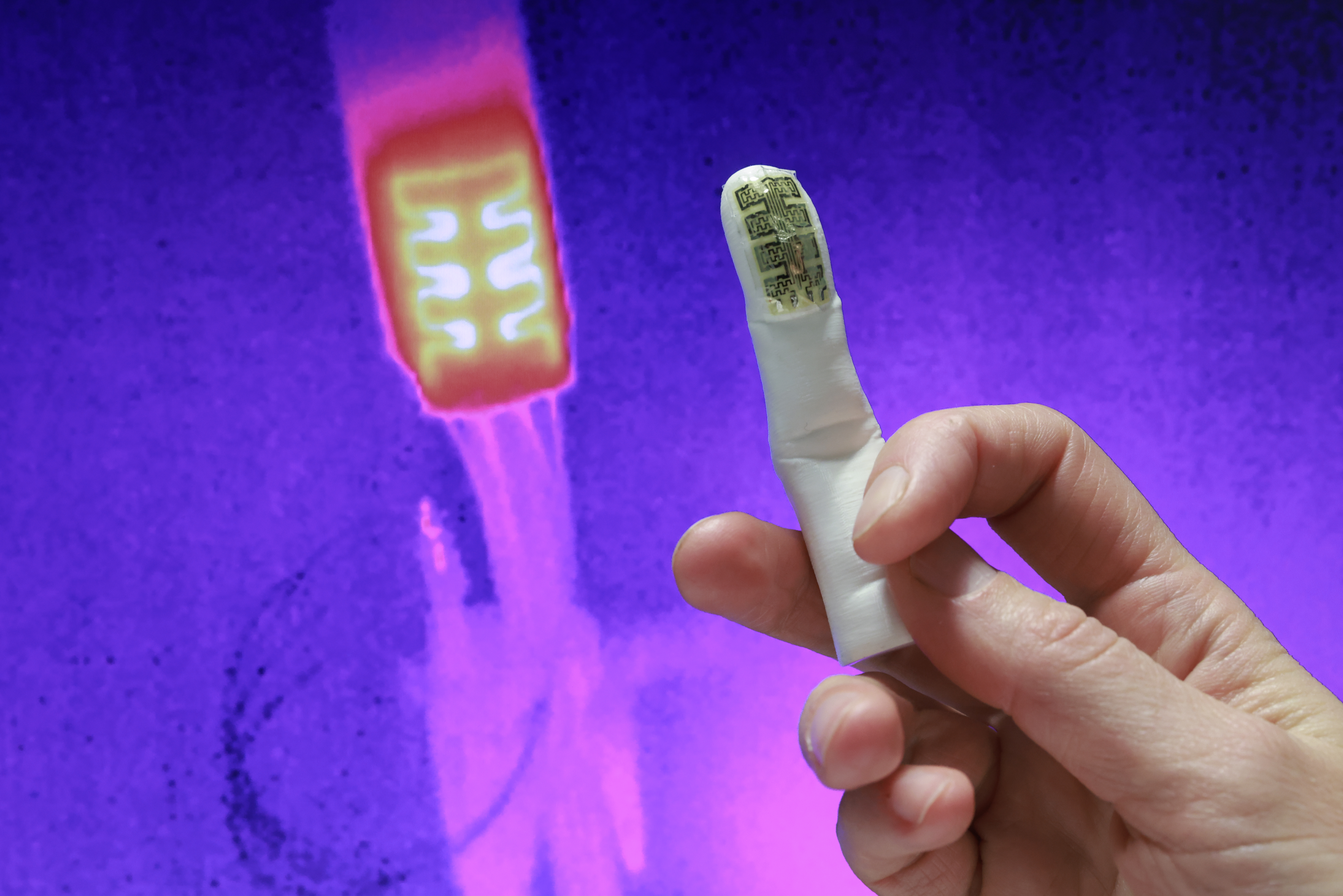 The bionic thermal sensor on the tip of a prosthetic finger, and its corresponding thermal image in the background as seen by a thermal camera