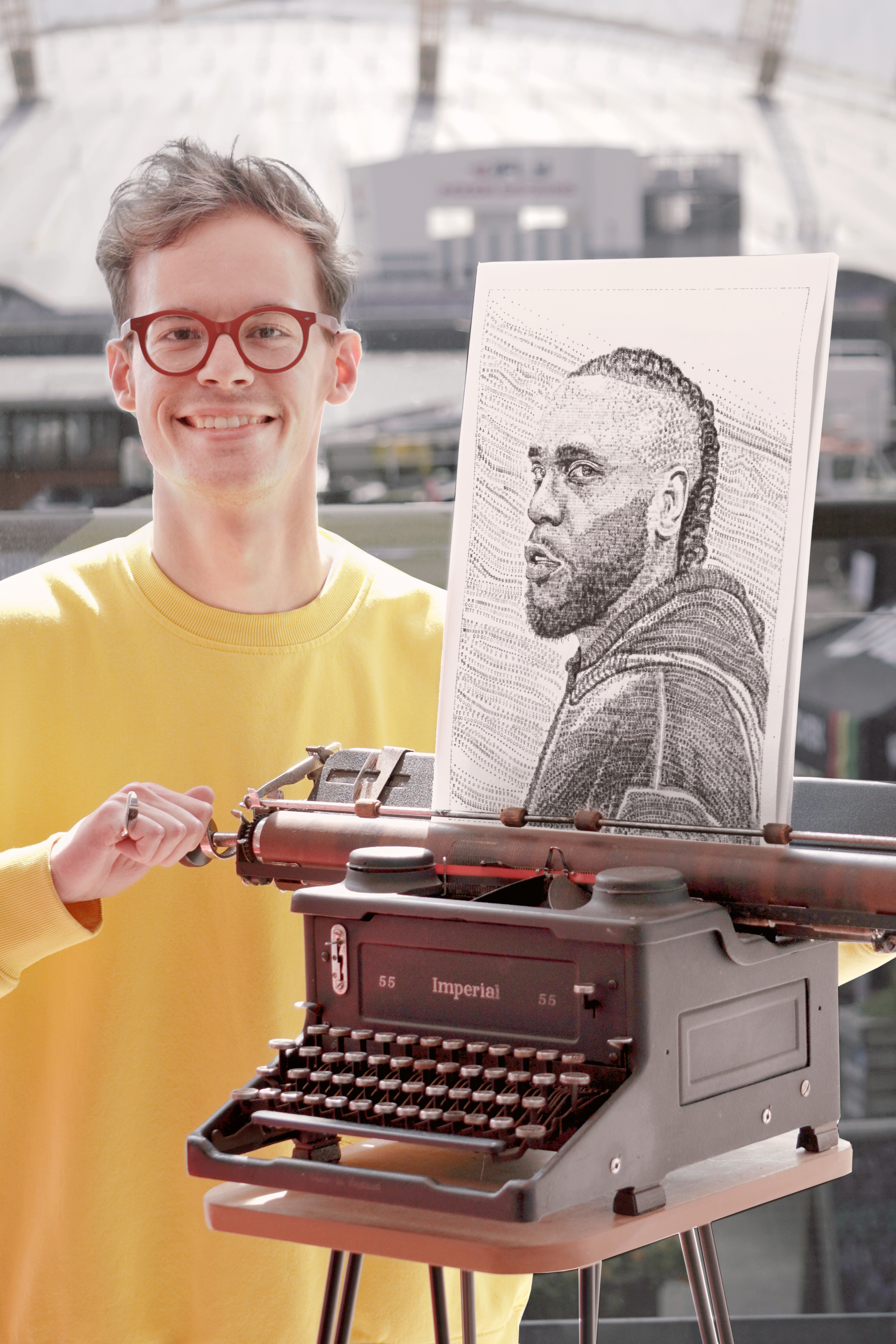 Man smiling at camera and standing next to a typewriter 