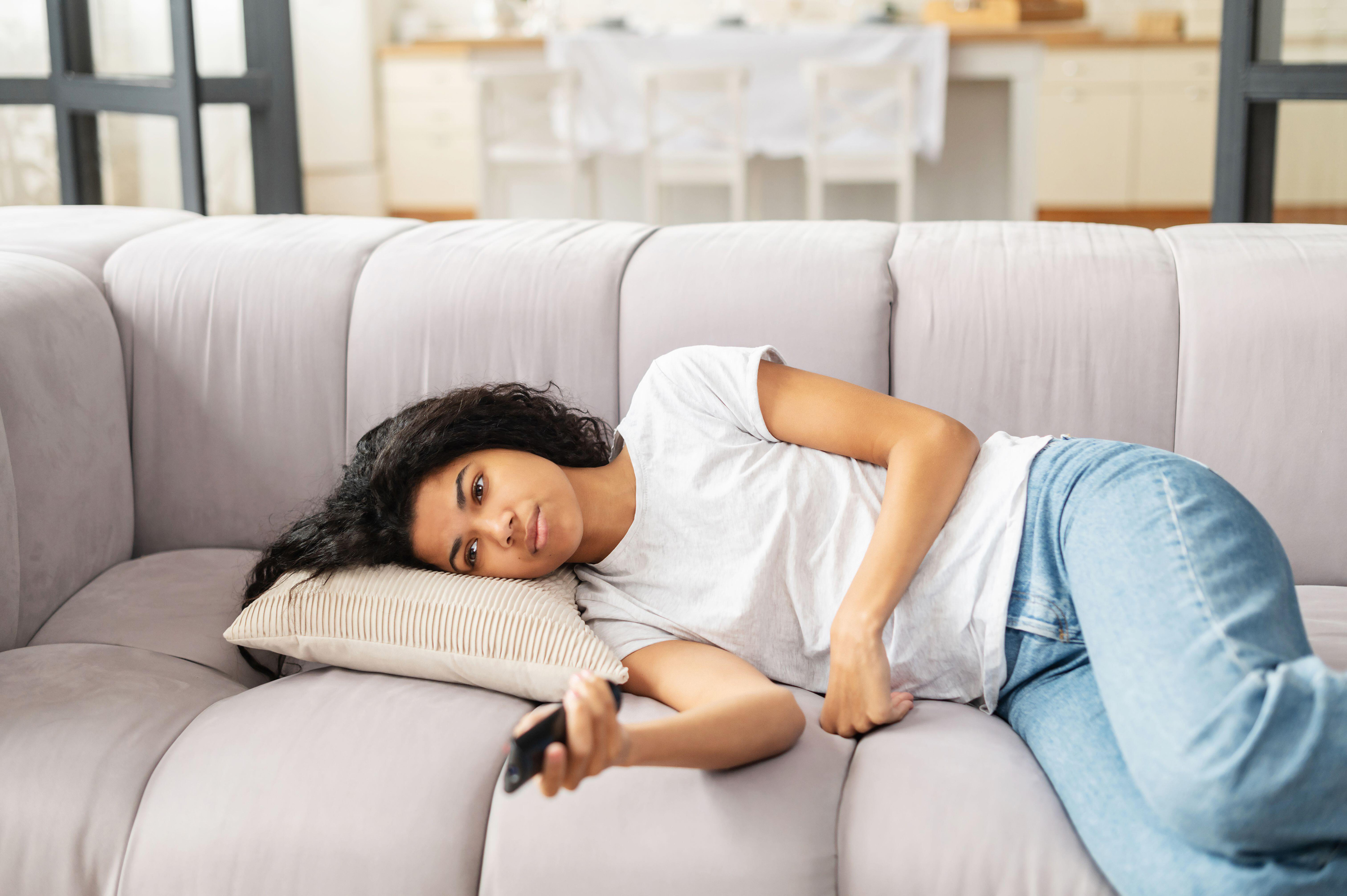 unhappy woman lying on sofa watching TV
