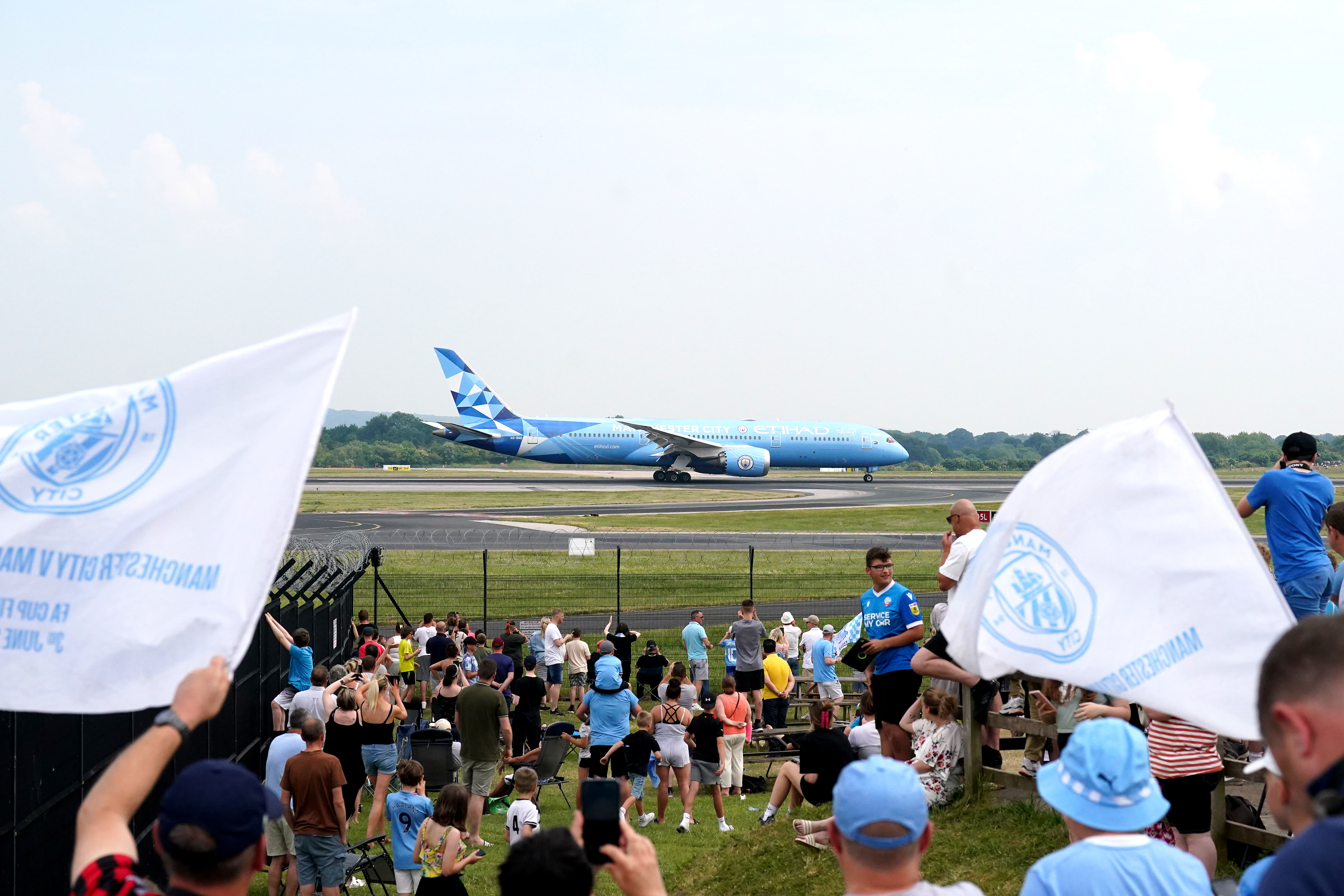 Manchester City fans celebrate as the Boeing 787-9 Dreamliner carrying the Manchester City players lands at Manchester Airport after their victory in the Champions League final 