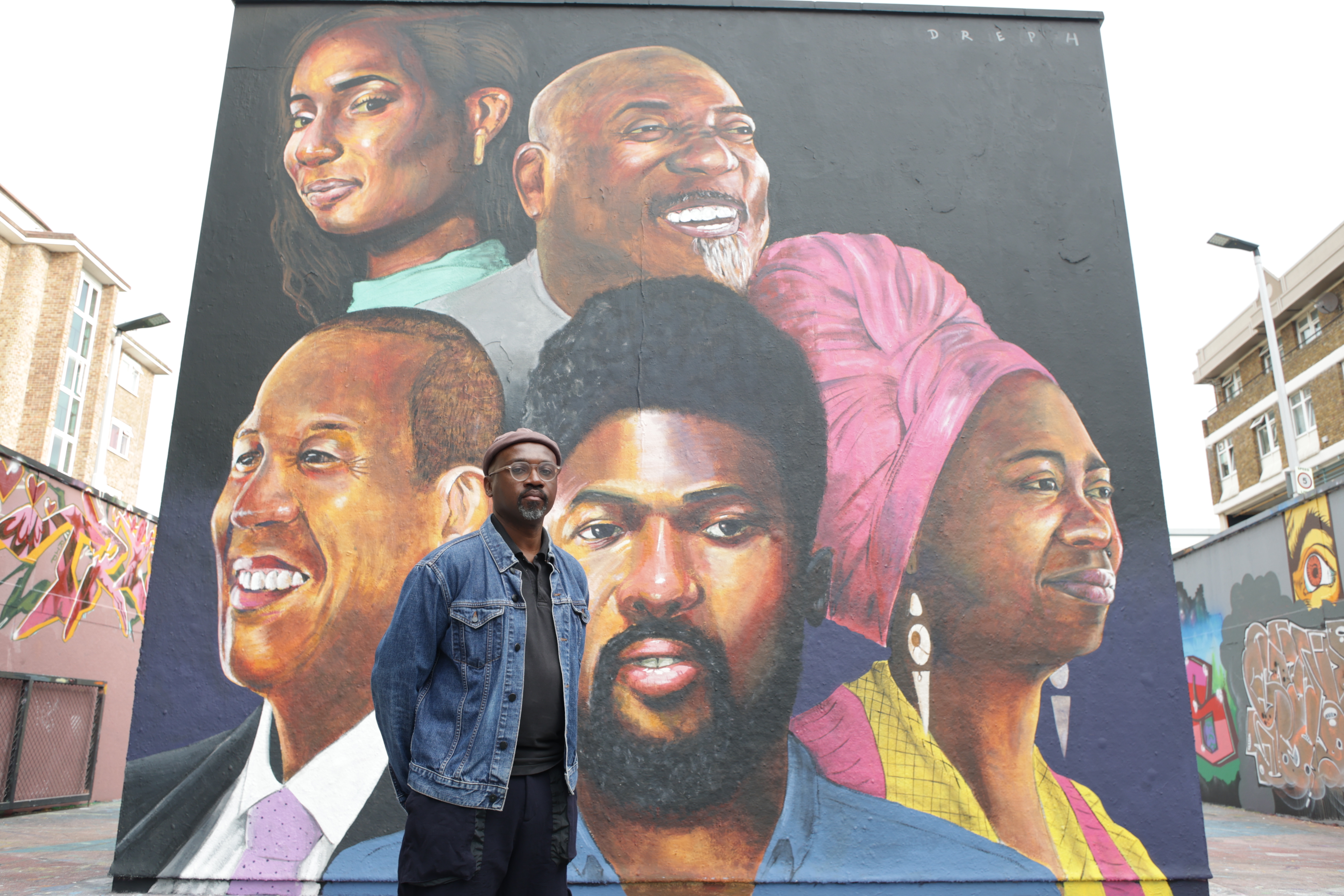 Neequaye Dreph standing in front of his mural depicting five individuals 