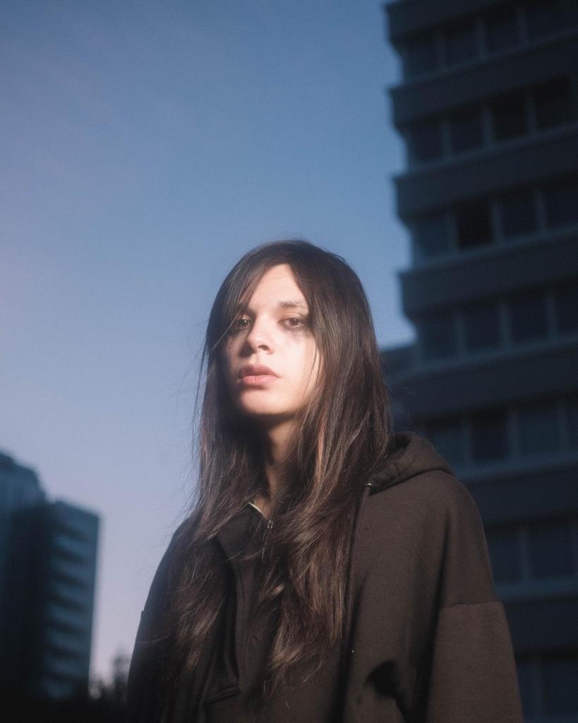 Enxi Erskine-Chang looking into the camera with the backdrop of a city skyline in twilight