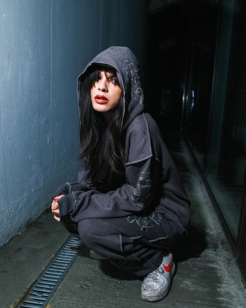 Enxi Erskine-Chang wearing a hoodie and crouching on the pavement in the dark