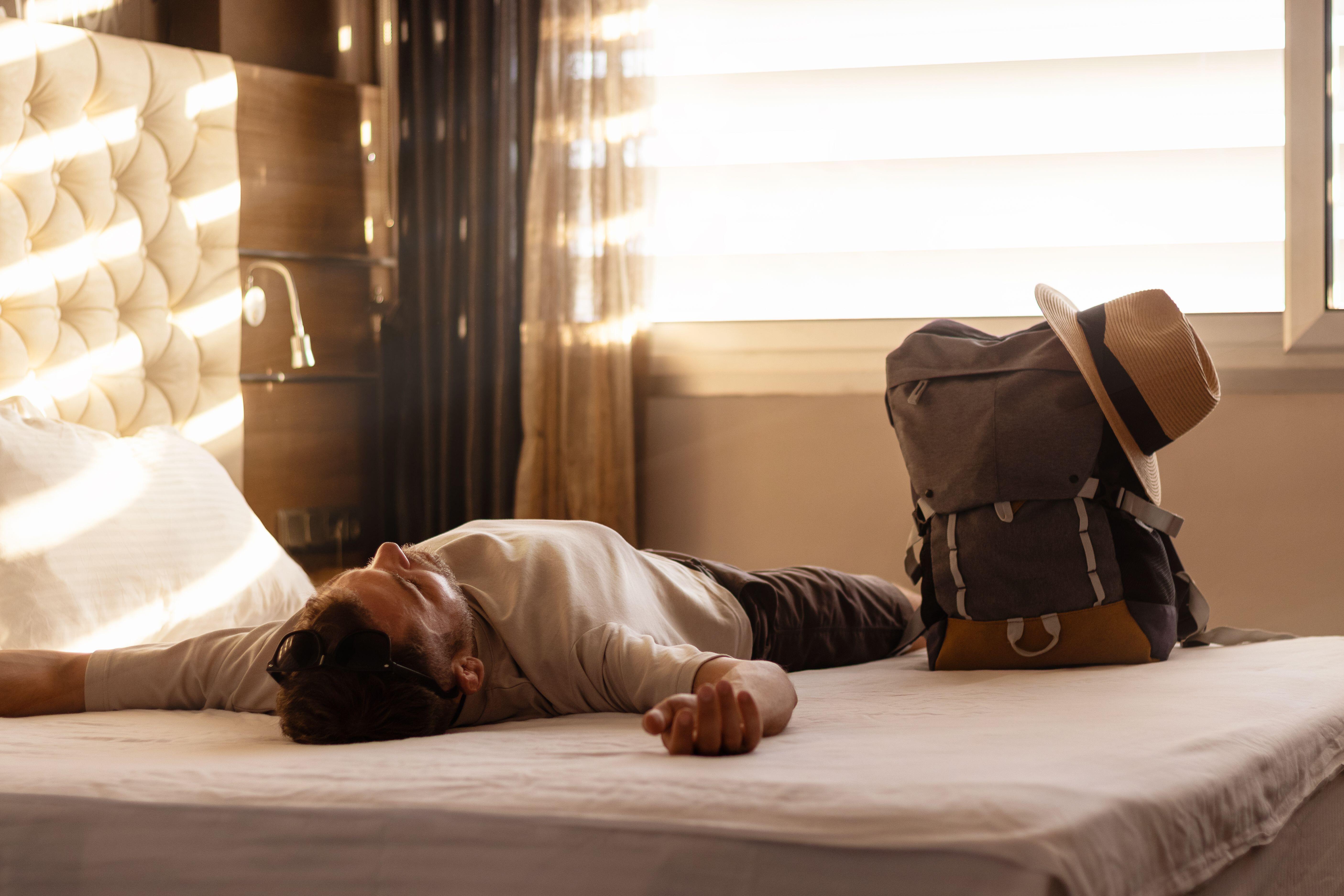Tired male tourist lying down after check-in on the bed in a hotel room