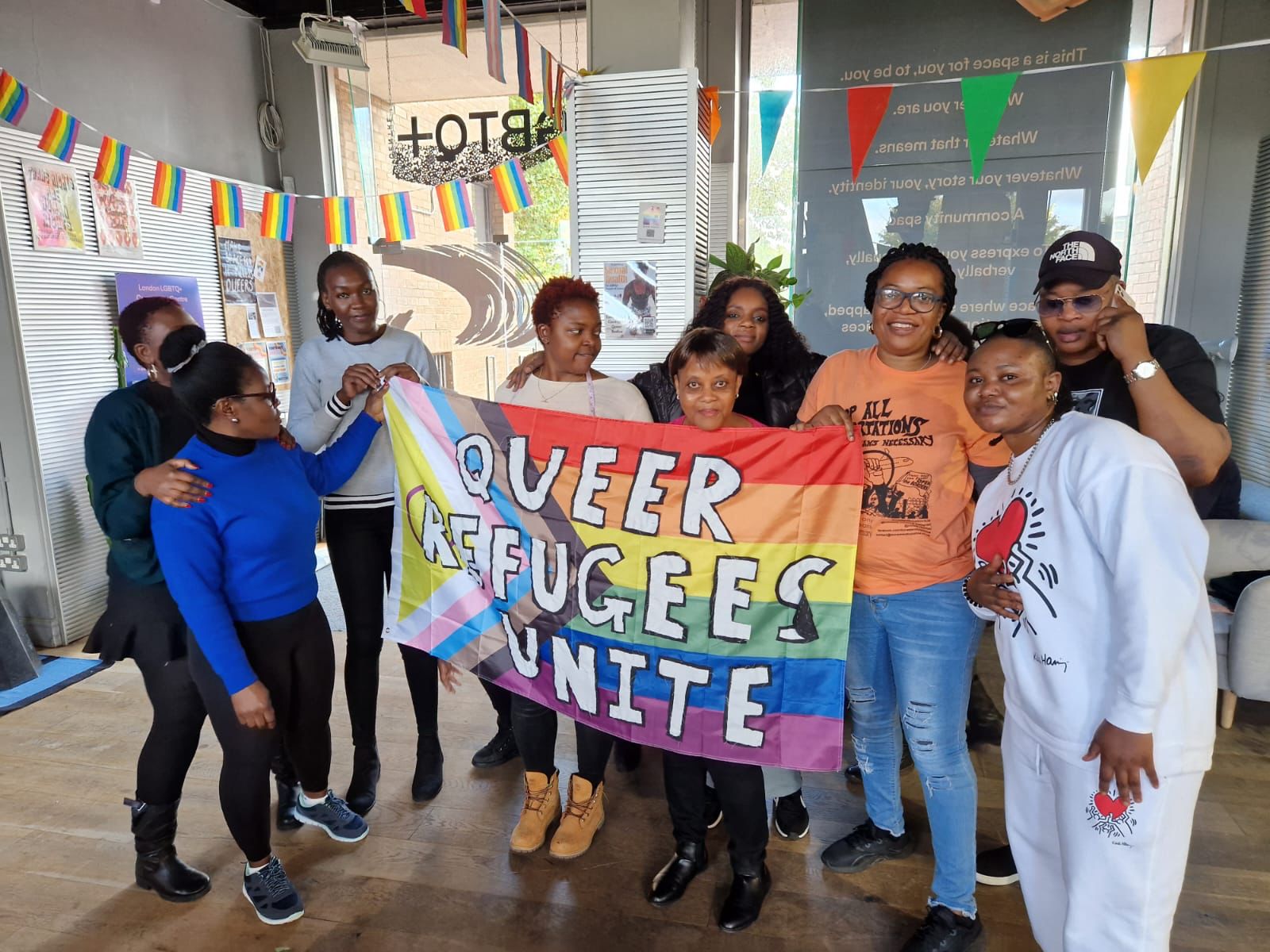 Group of members from Queer Refugee Unite holding an LGBTQ+ banner