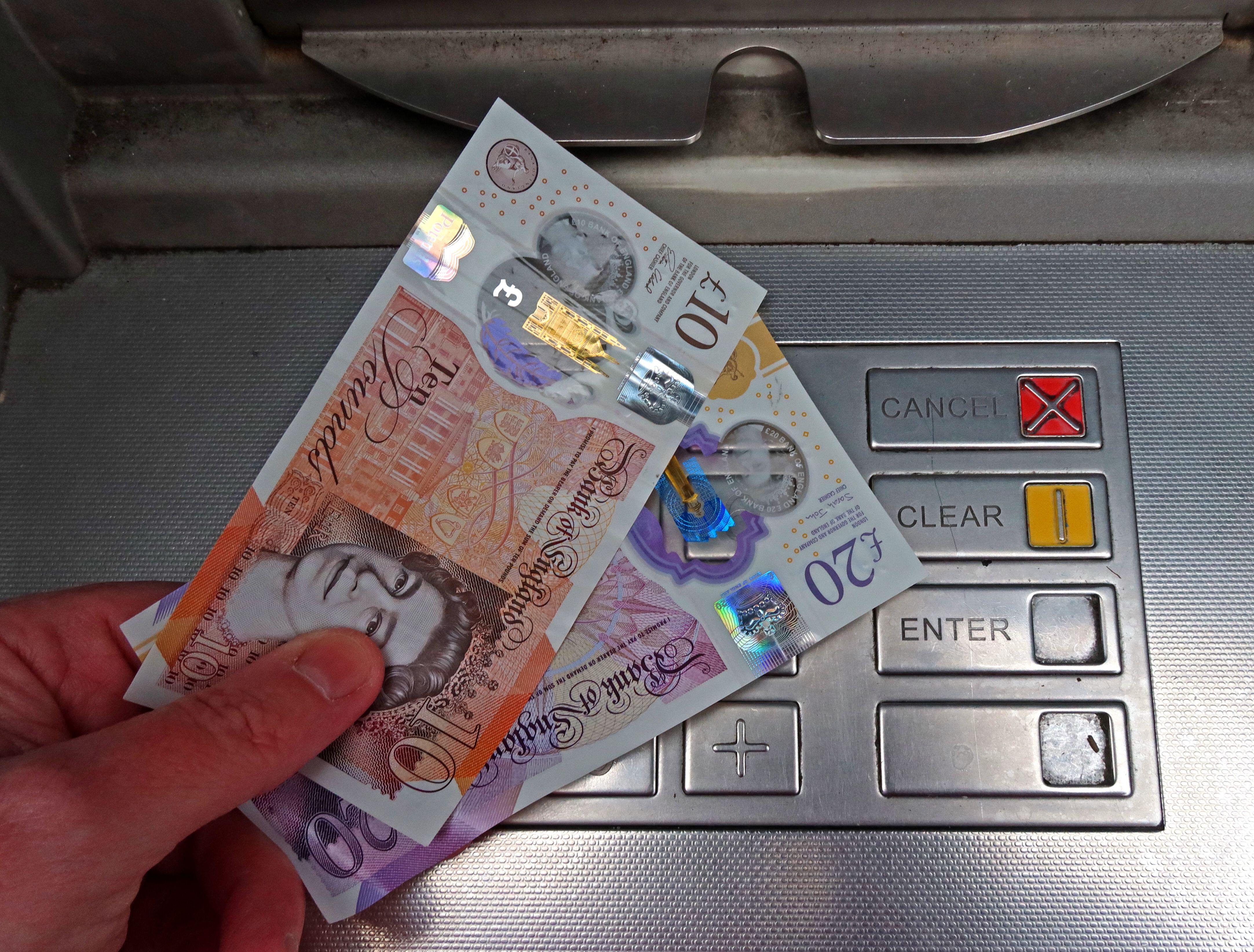 A person holding £30 by a cash machine