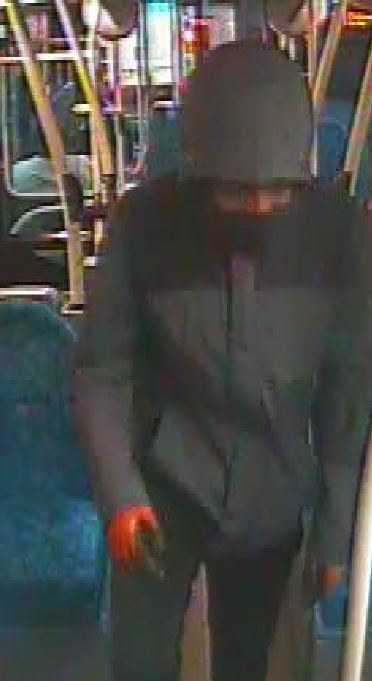 A man wearing a dark coat with the lower half of his face covered standing on a bus.