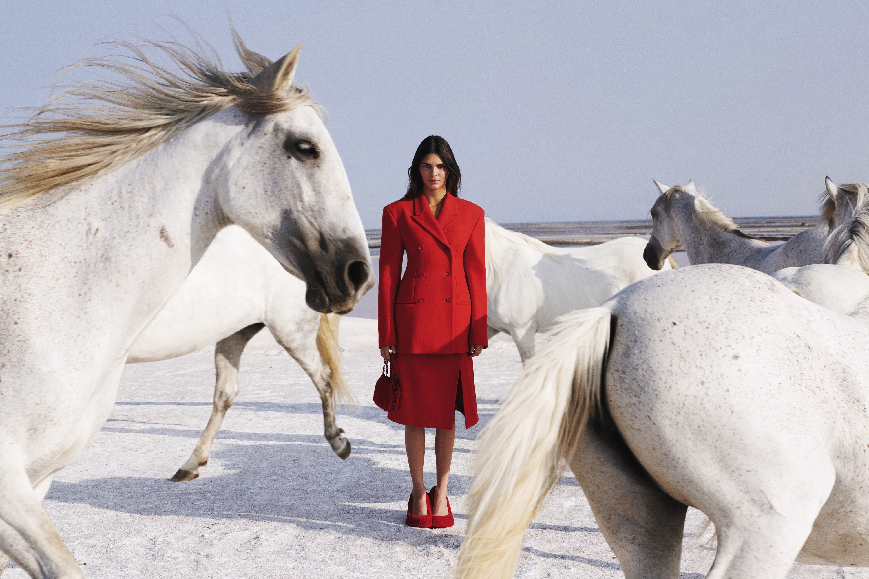 Kendall Jenner wearing red skirt, blazer and shoes, surrounded by white horses as part of promotional campaign