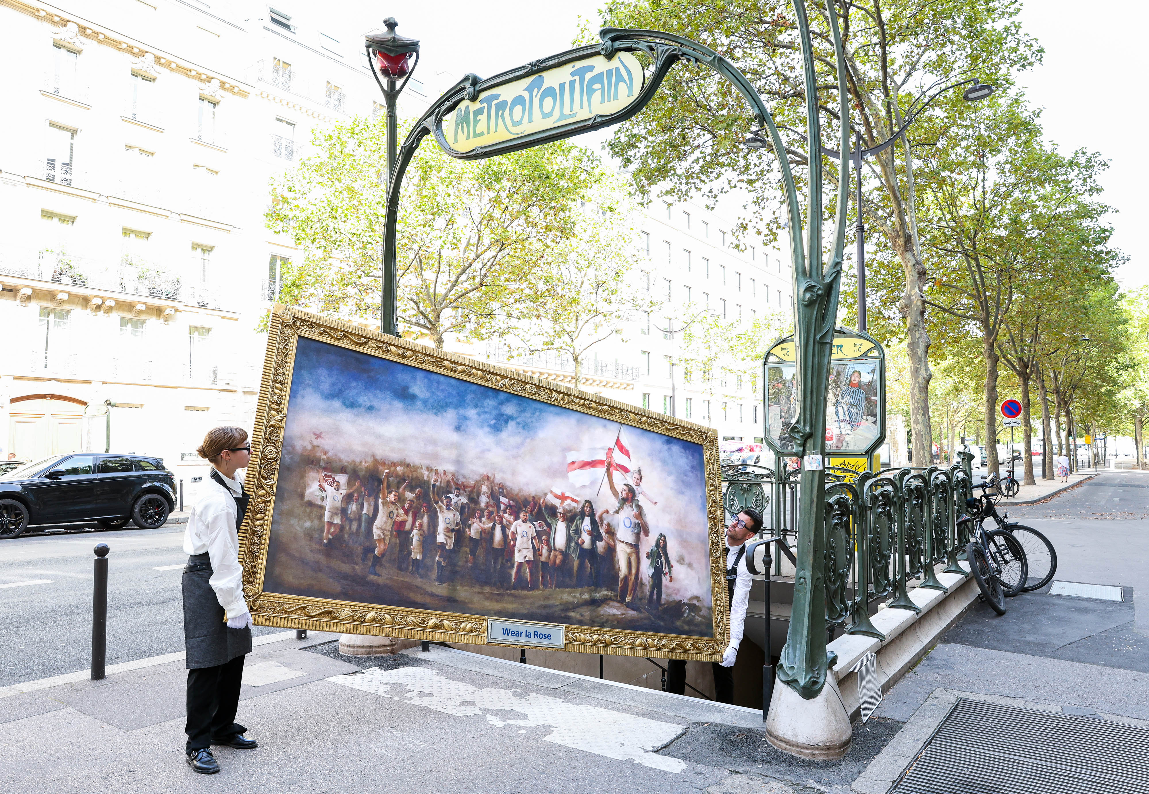Two people carrying the painting trying to take it down the stairs of Paris' Metro 