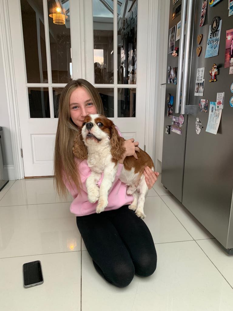 Young girl holds her dog whilst kneeling on the ground