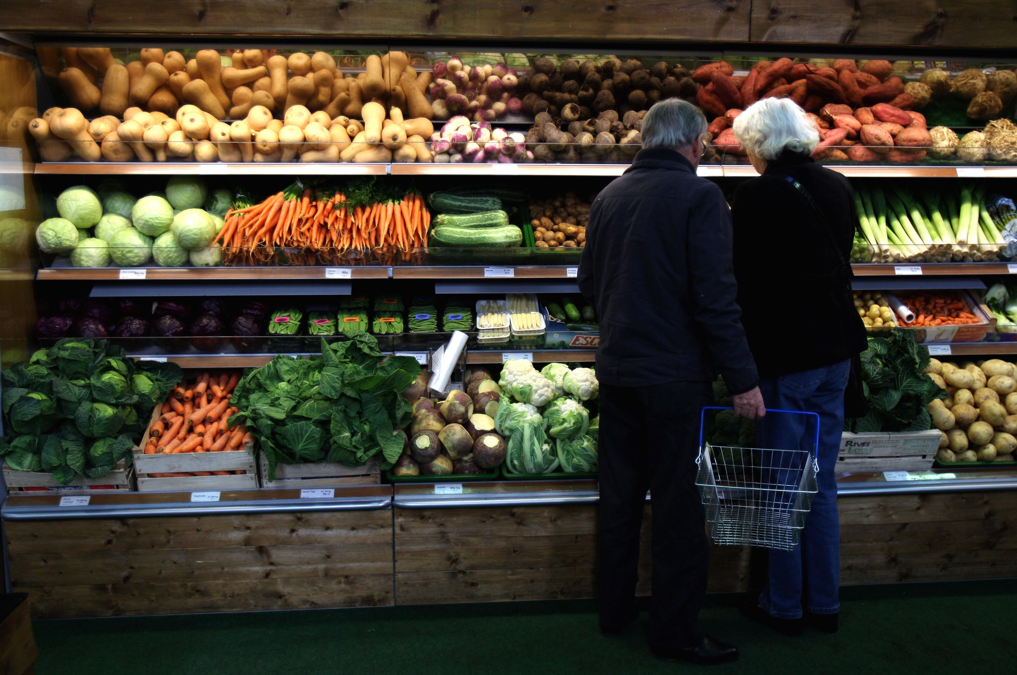 A couple standing looking at rows of vegetables in a supermarket
