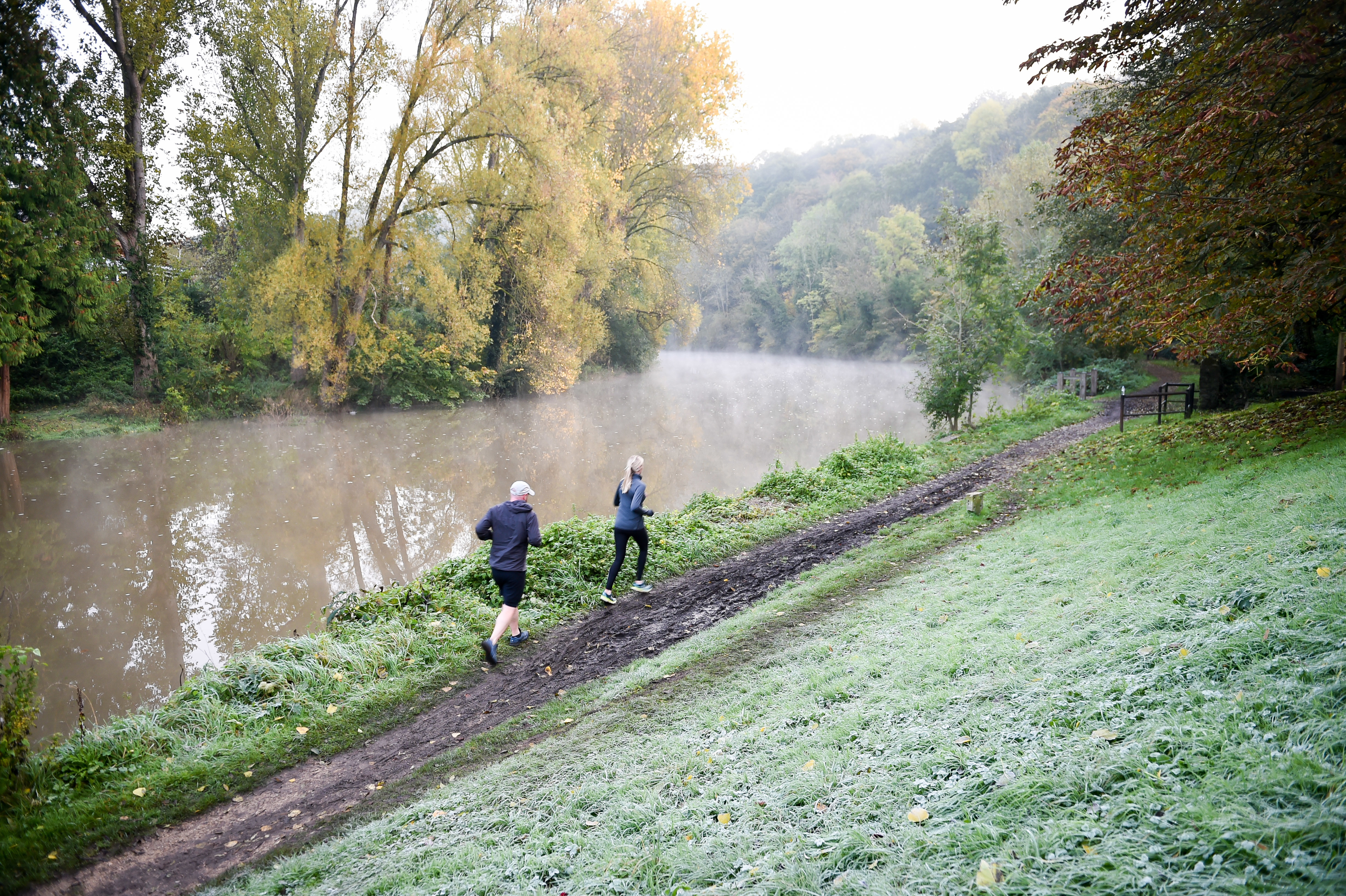 Two people jogging alongside a river on a winter day