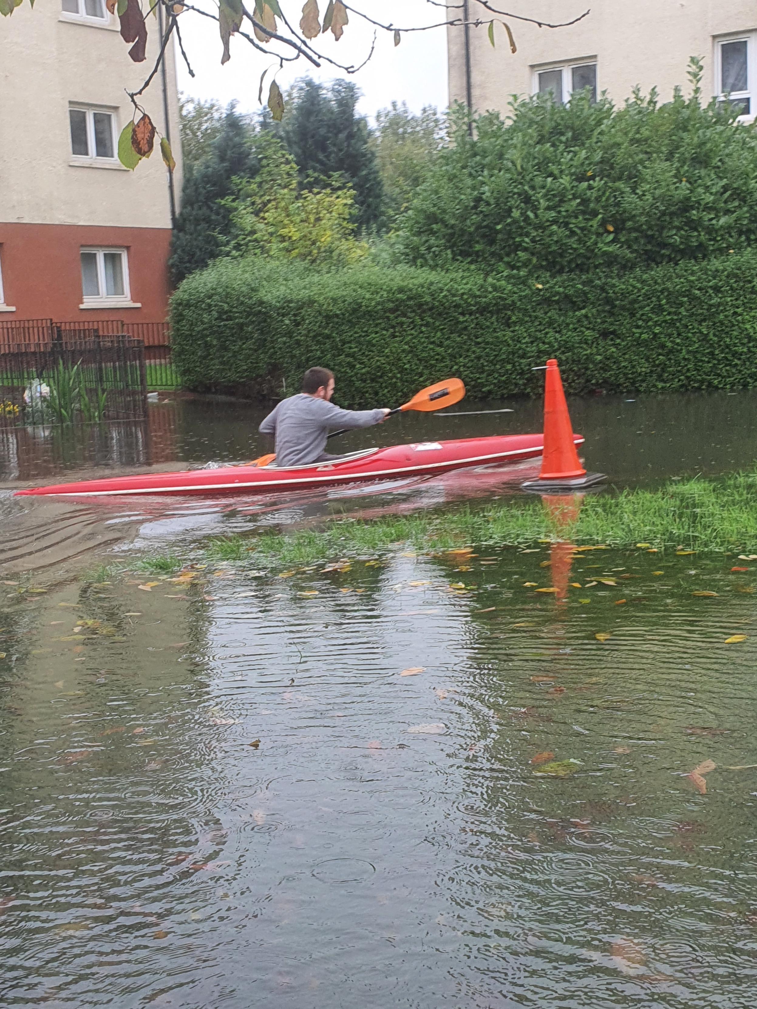 Man kayaking on a residential road that is flooded