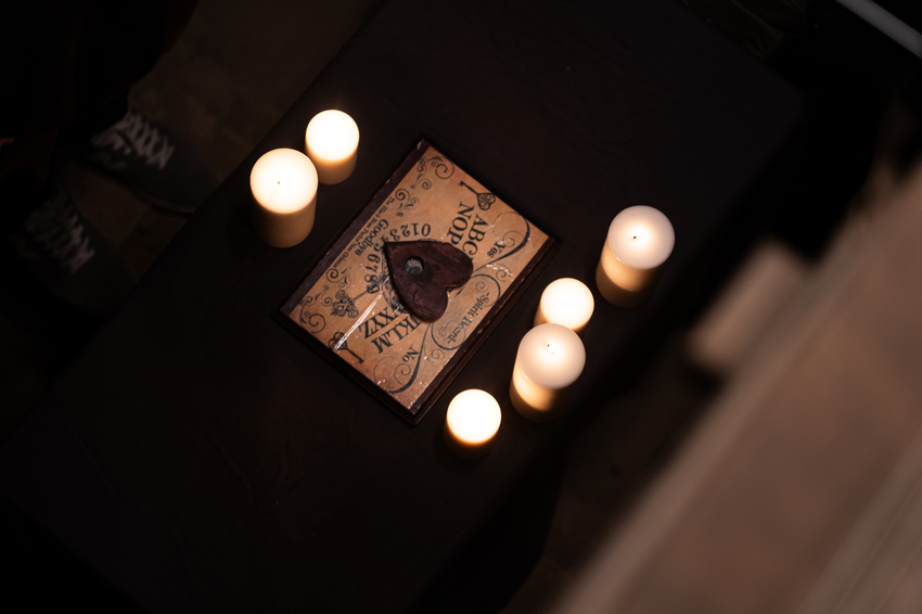 Spirit Board surrounded by candles, seen from above. Jack's feet barely in shot.