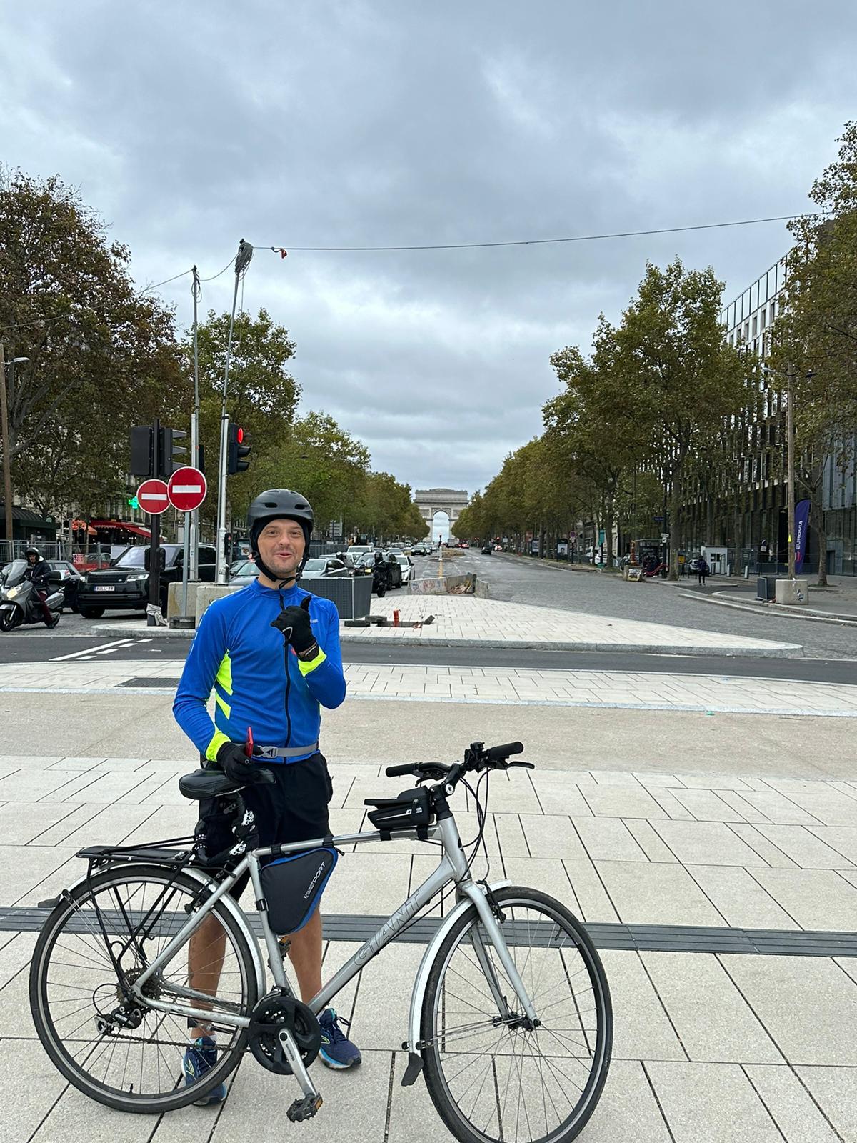Cyclist stands with his bike with the Arc de Triomphe monument in the far distance