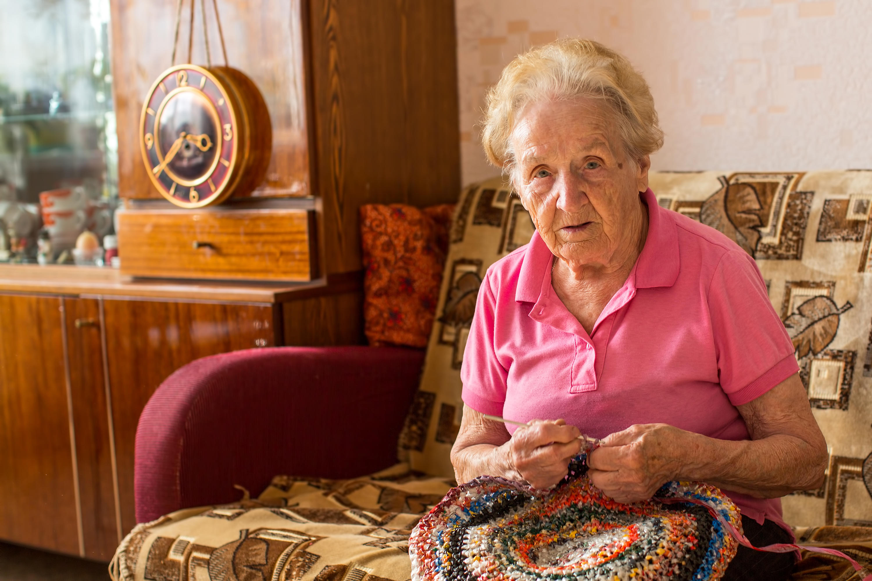 n elderly woman sitting in her room and knitting rug