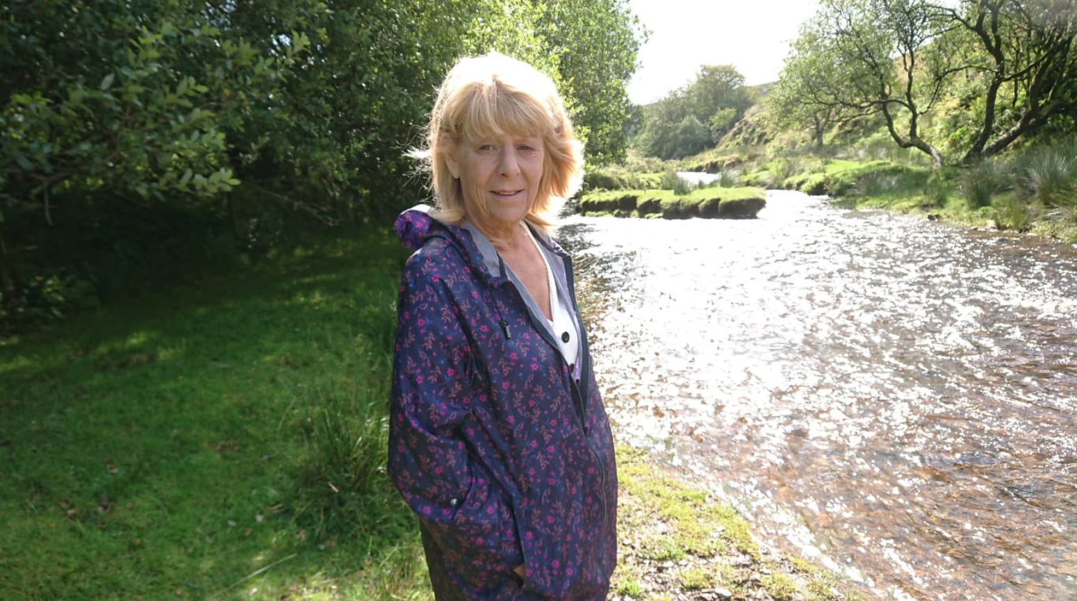 Woman in purple jacket stands by a rive
