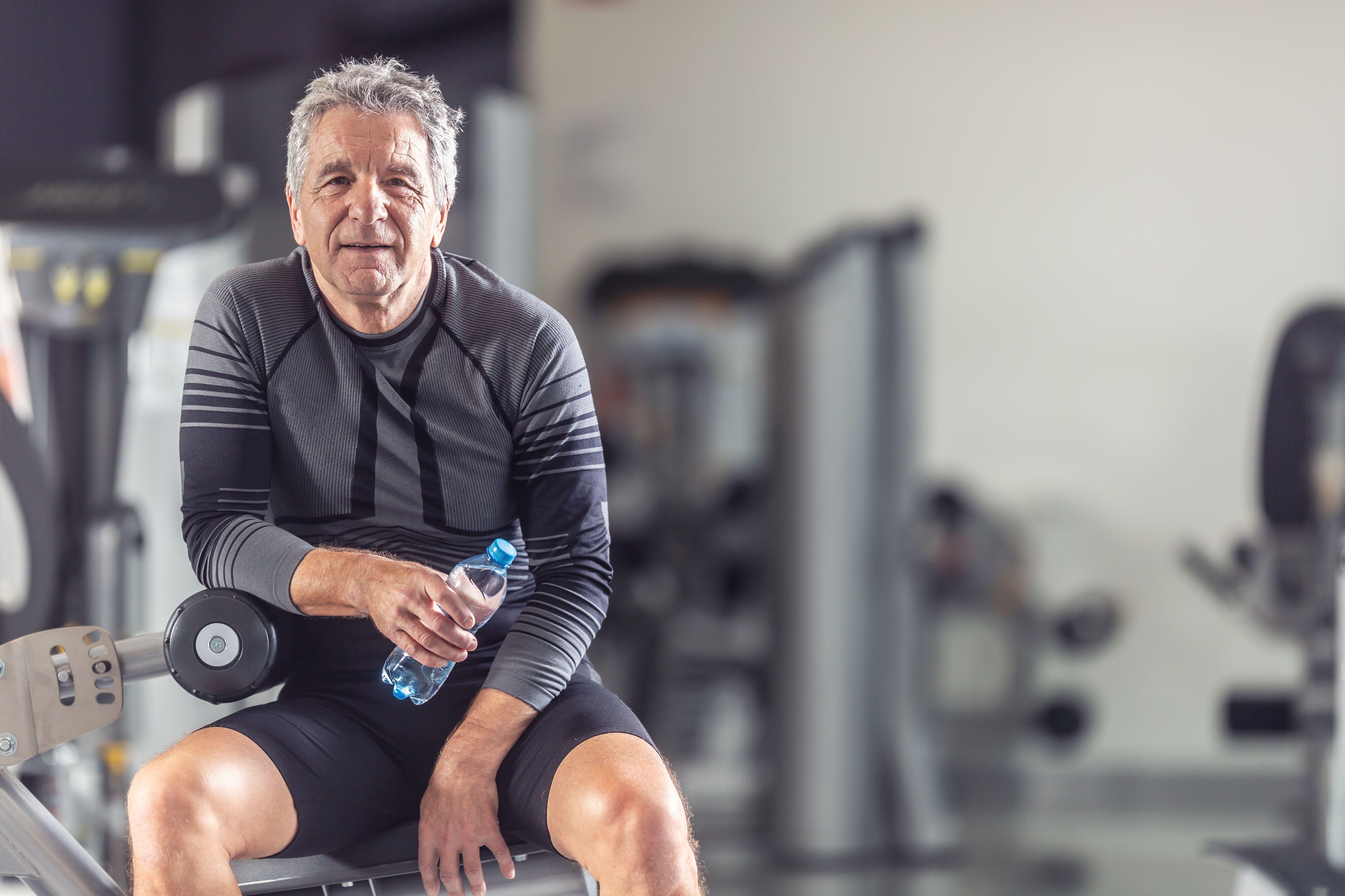 Pensioner keeps himself fit working out in a gym, resting with a bottle of water.