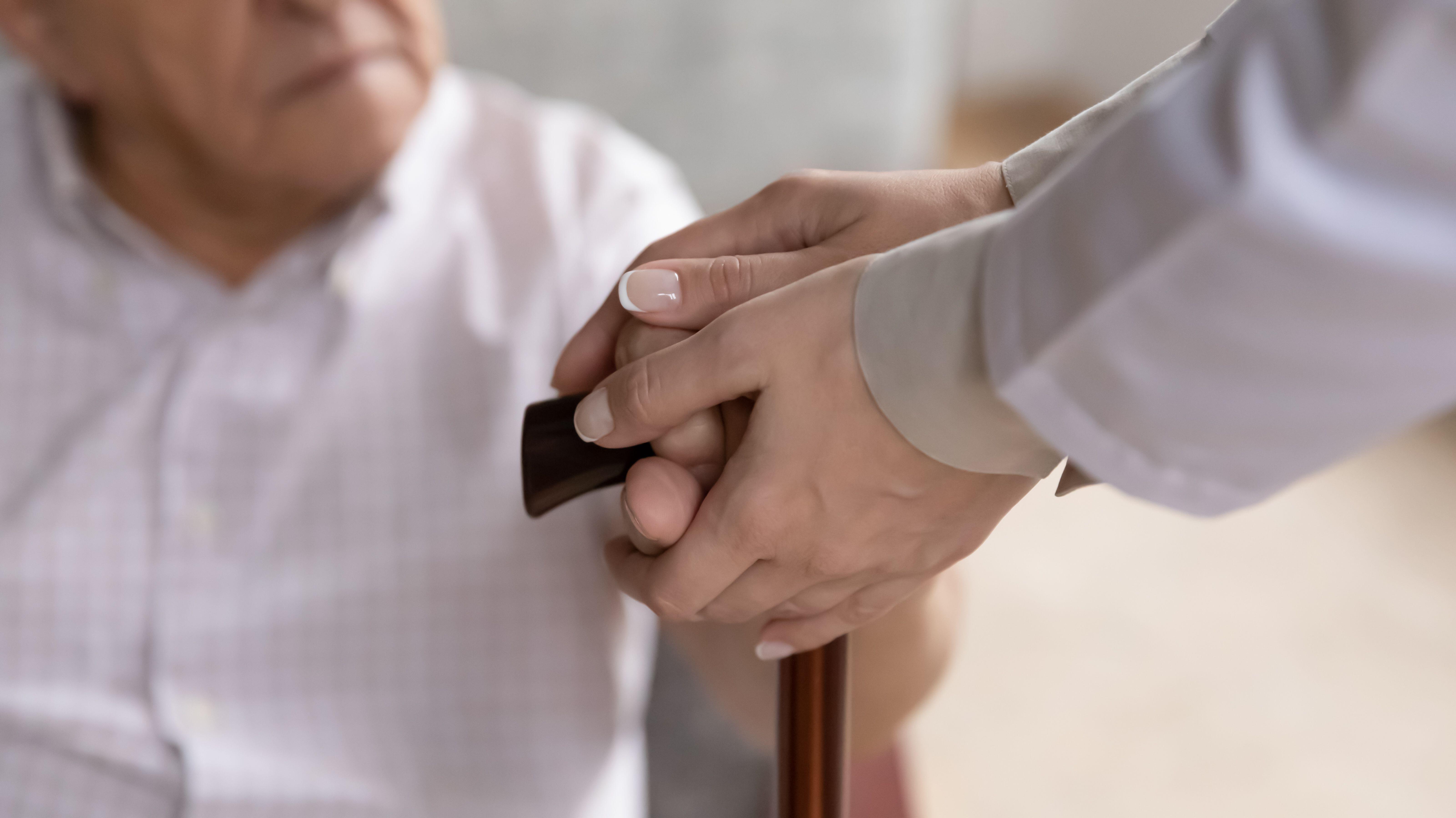 Carer hands holding old patient arms touch walking stick closeup (Alamy/PA)