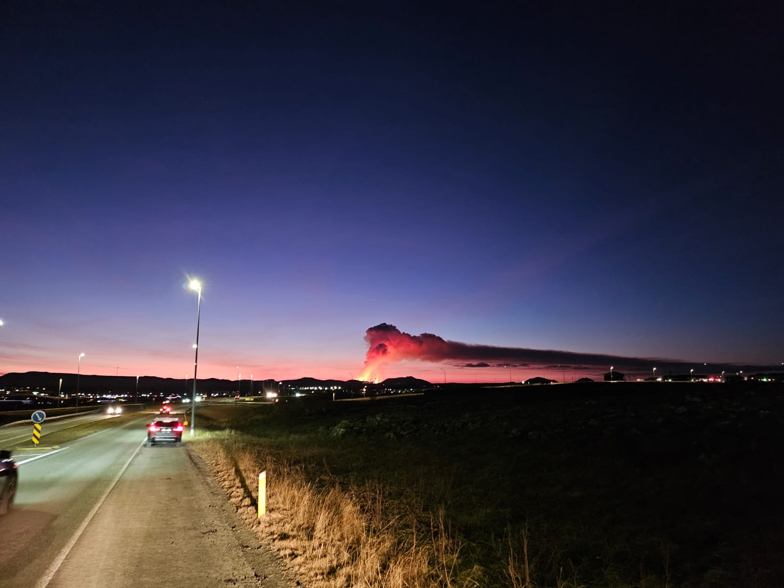 A picture of the Iceland volcano erupting in the distance, with a plume of smoke rising in the air