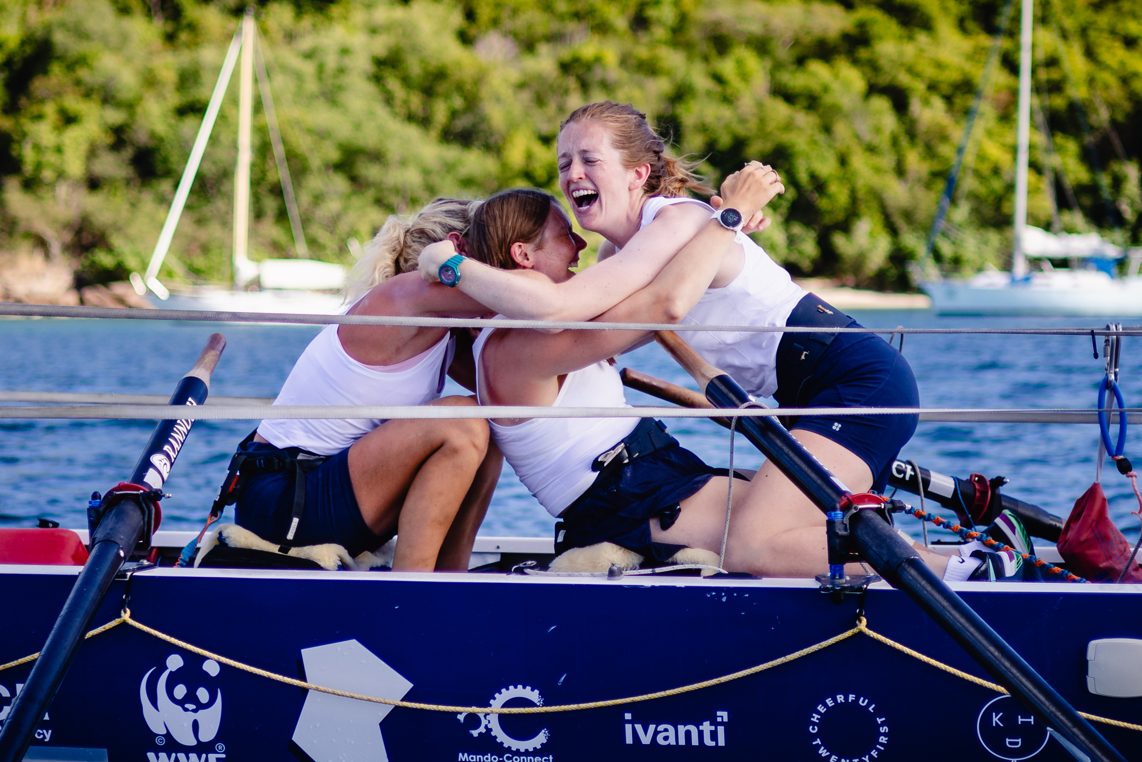 Three woman hug on a row boat after completing a 3,000-mile race