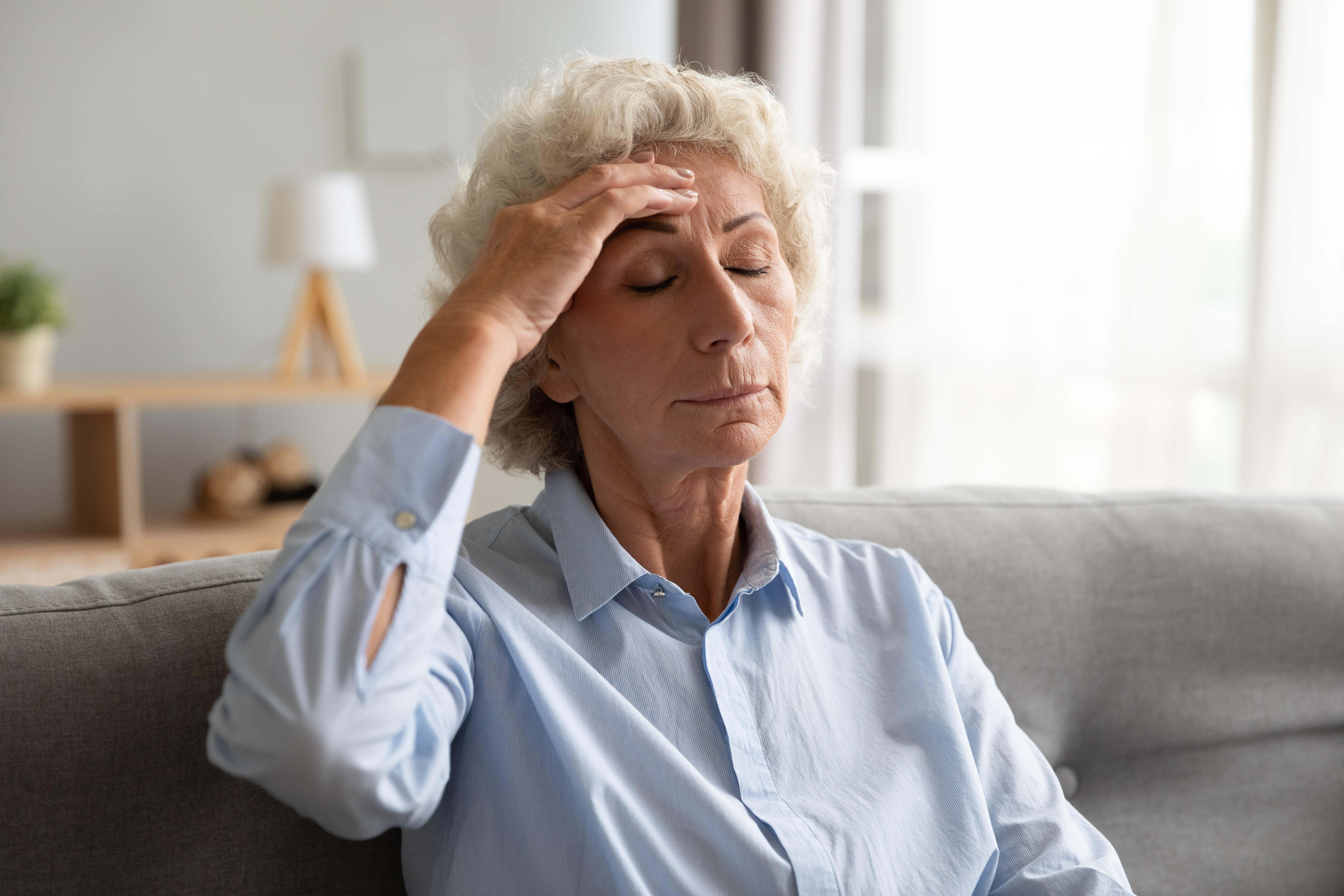 Upset senior lady feeling dizzy having headache sit on sofa