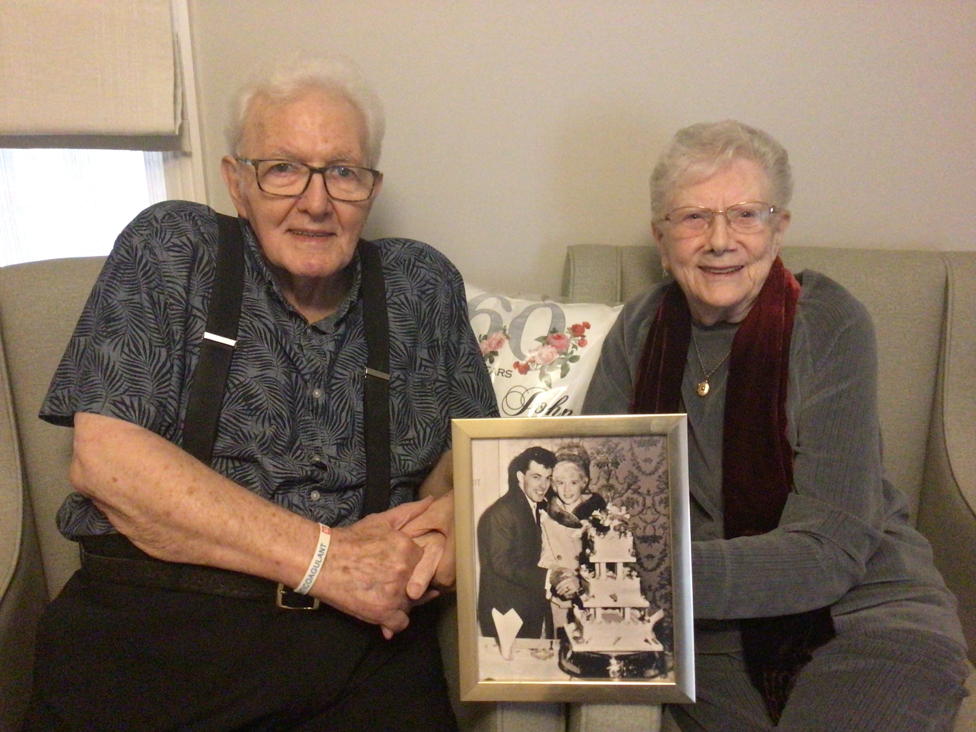 Elderly couple hold a picture of themselves at their wedding