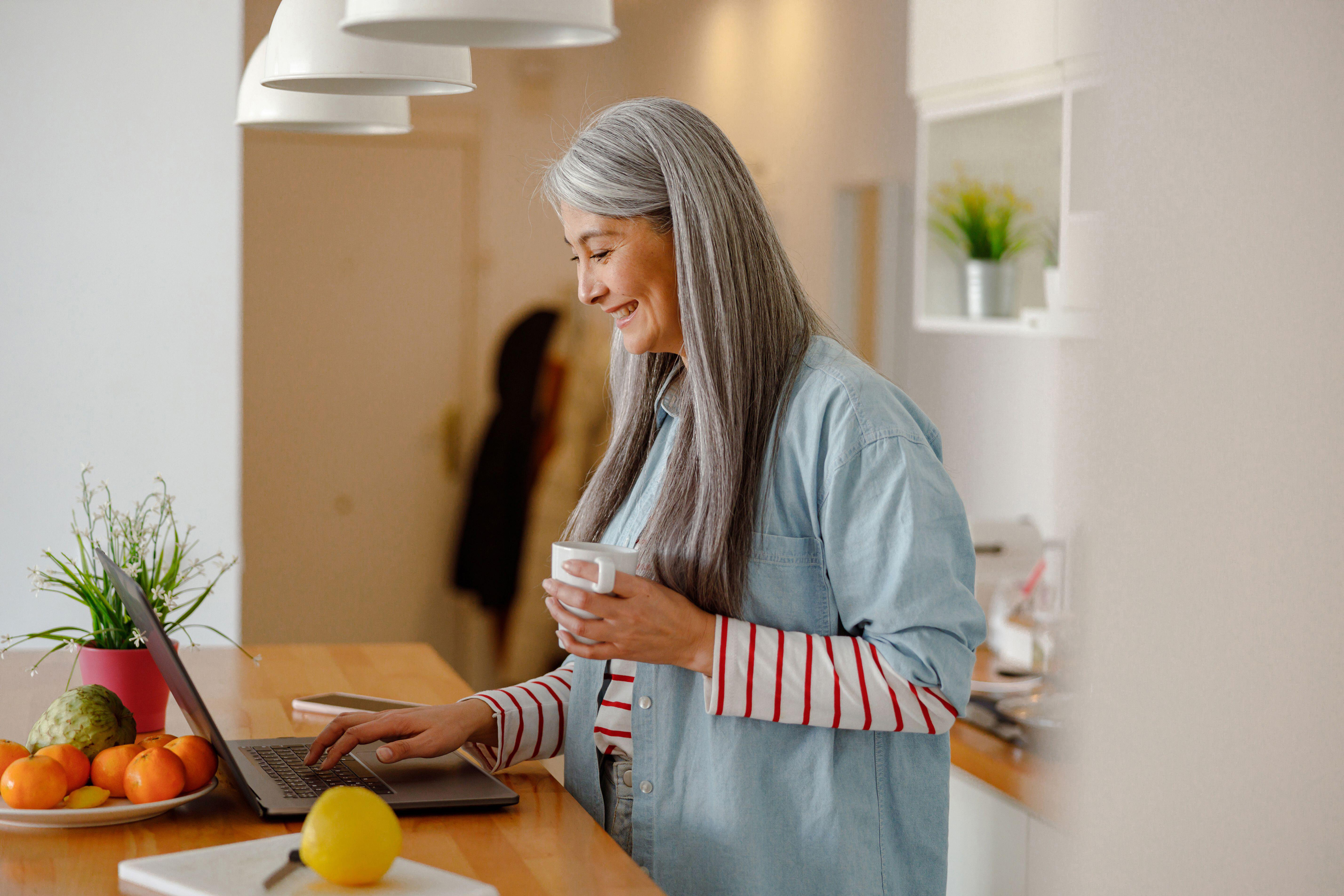 Woman drinking coffee in kitchen while using keyboard