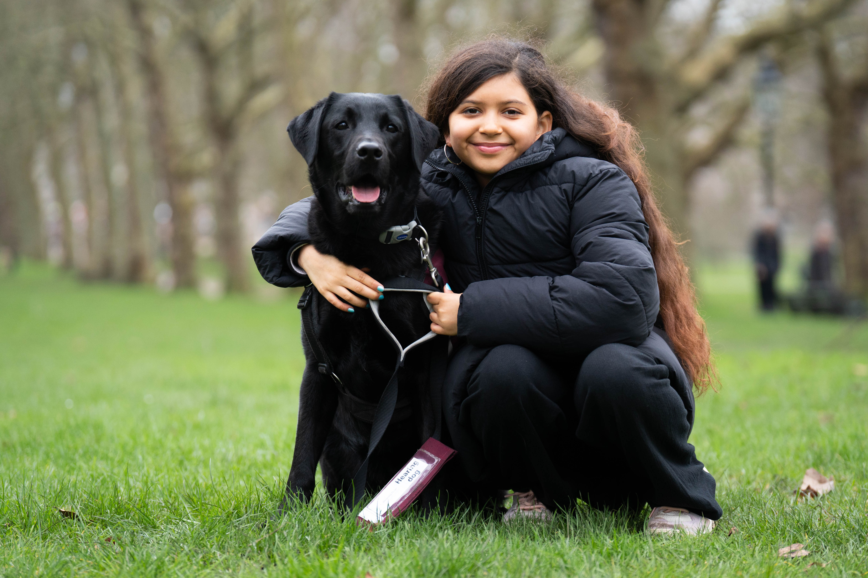 A girl kneeling on the ground with her arms around her dog 