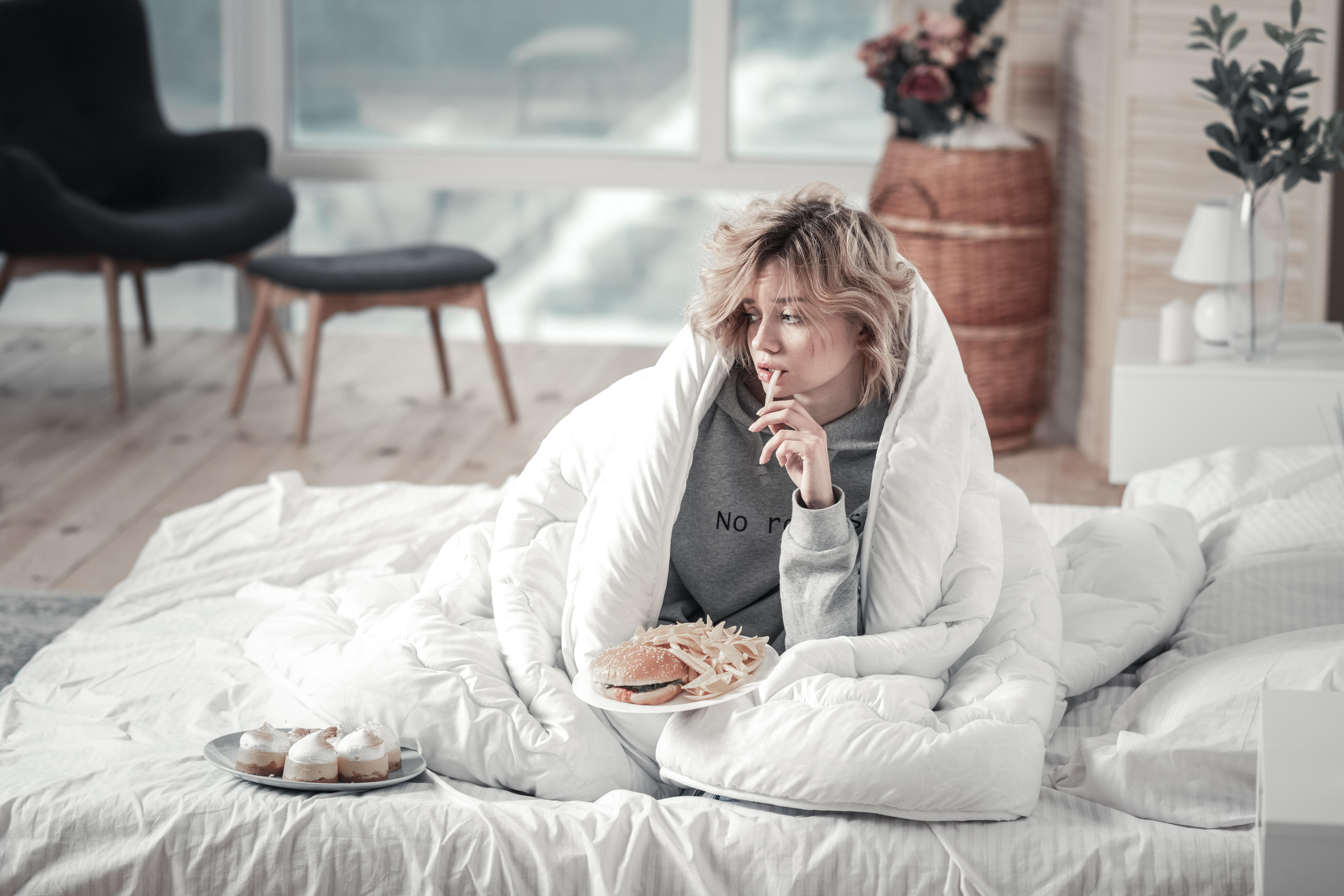 T1J40E Woman eating junk food in her bed after breakup with boyfriend