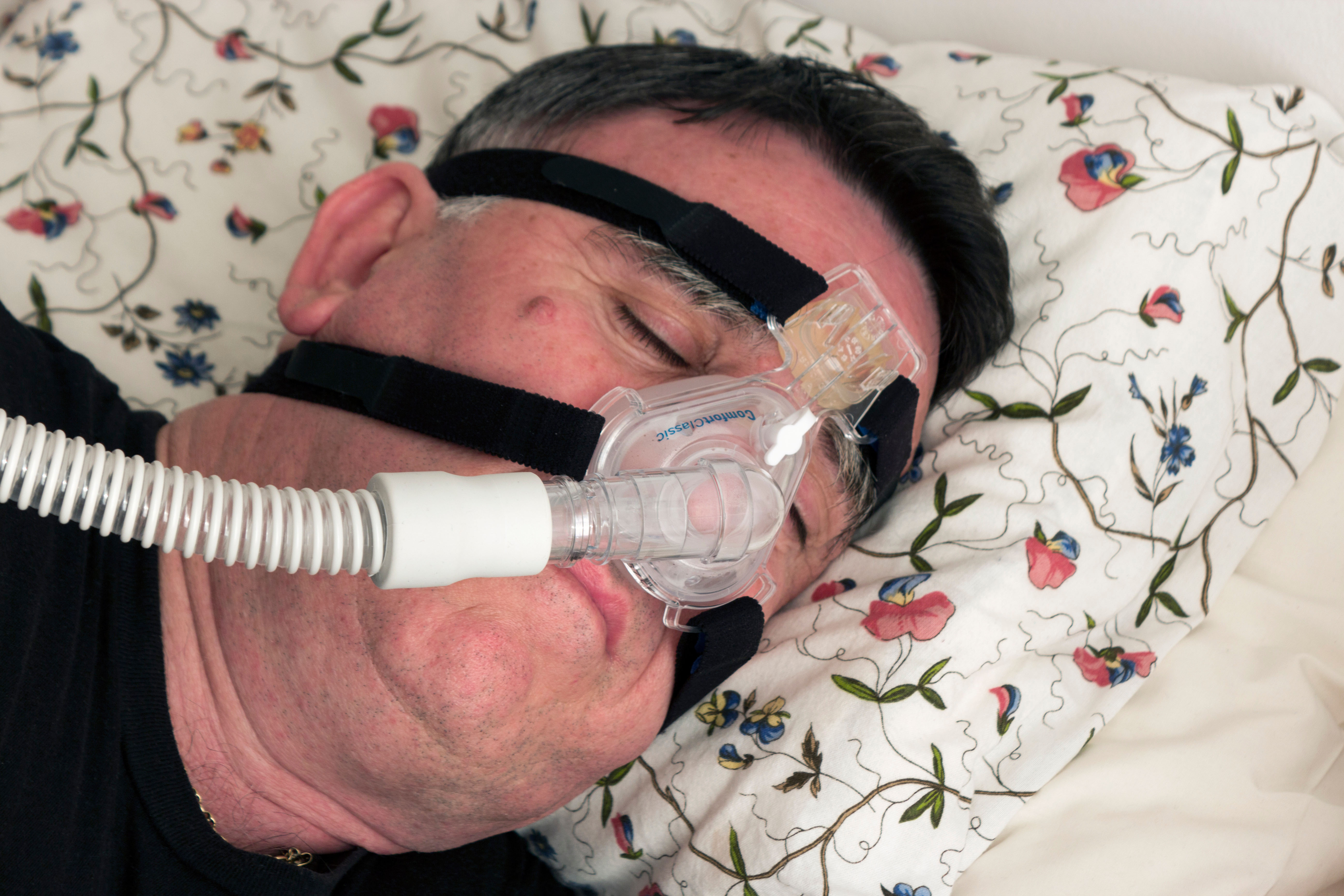 Man using a CPAP face mask and machine used for the treatment of sleep apnea.