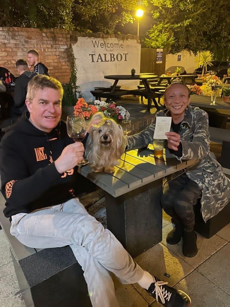A photo of Adrian Chapman and Steven Sin sitting together at a pub and smiling at the camera 