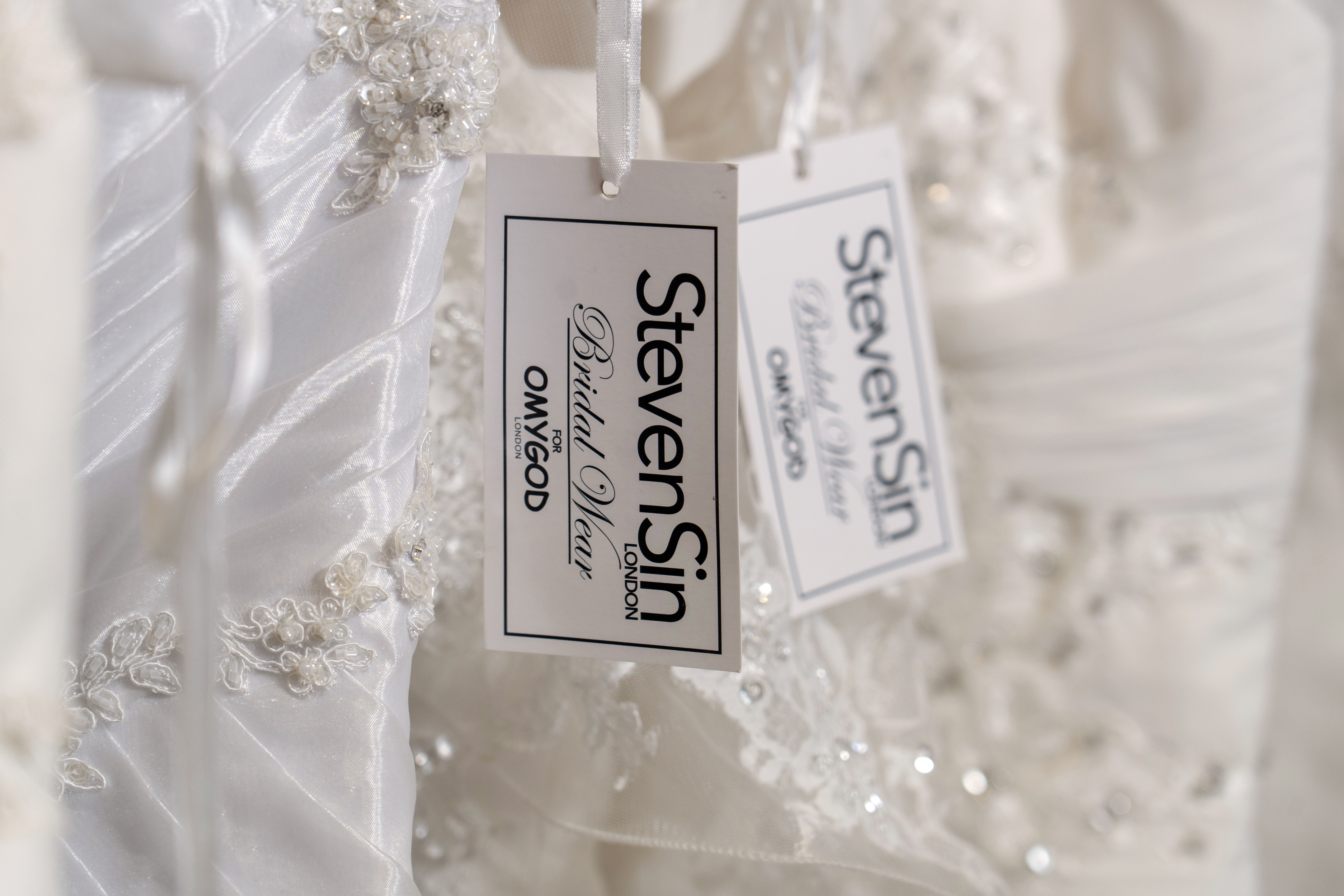 A photo zoomed in on a tag on the wedding dresses reading 'Steven Sin' 