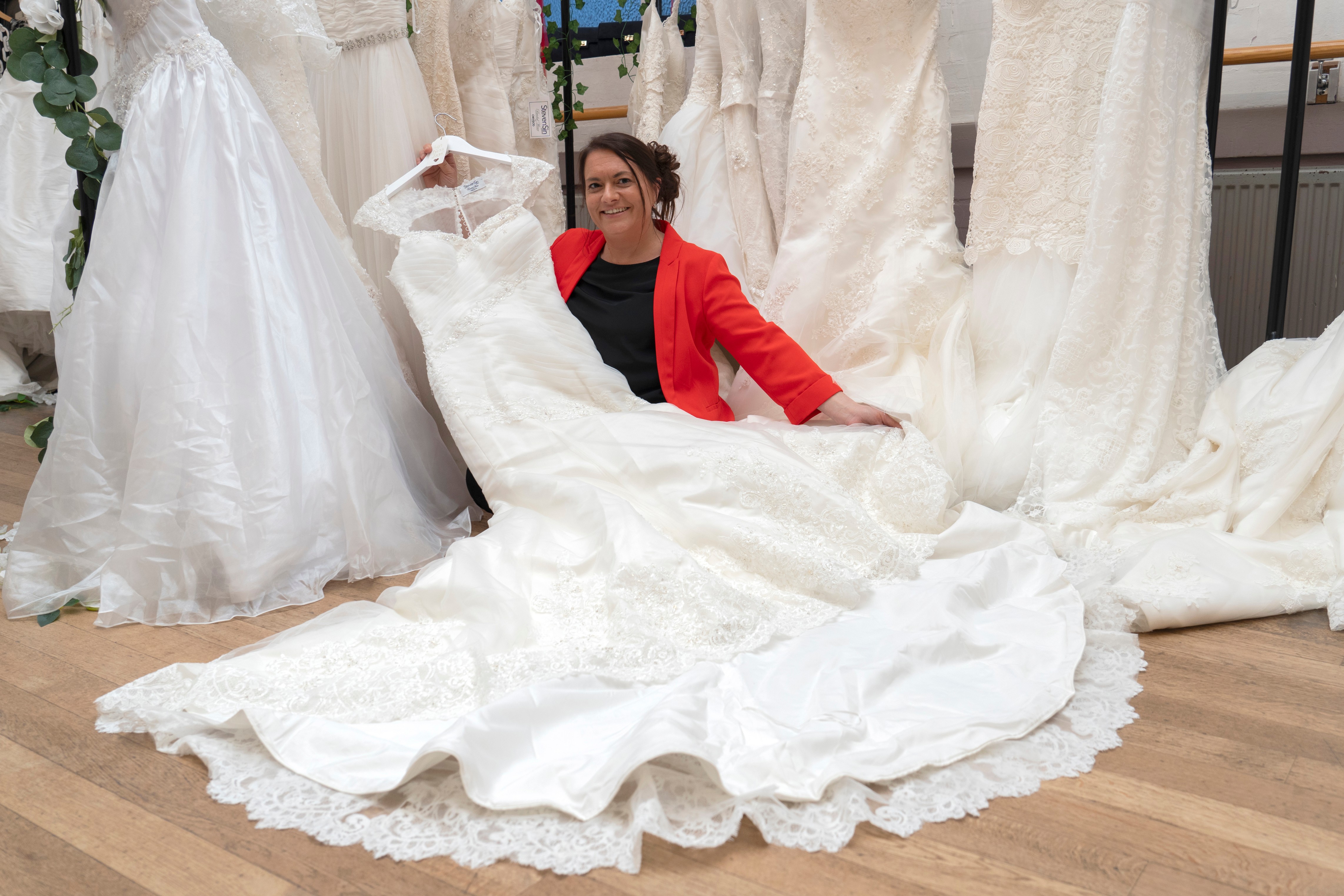 A photo of Sally Todd, the BHF shop manager, holding up one of the wedding dresses