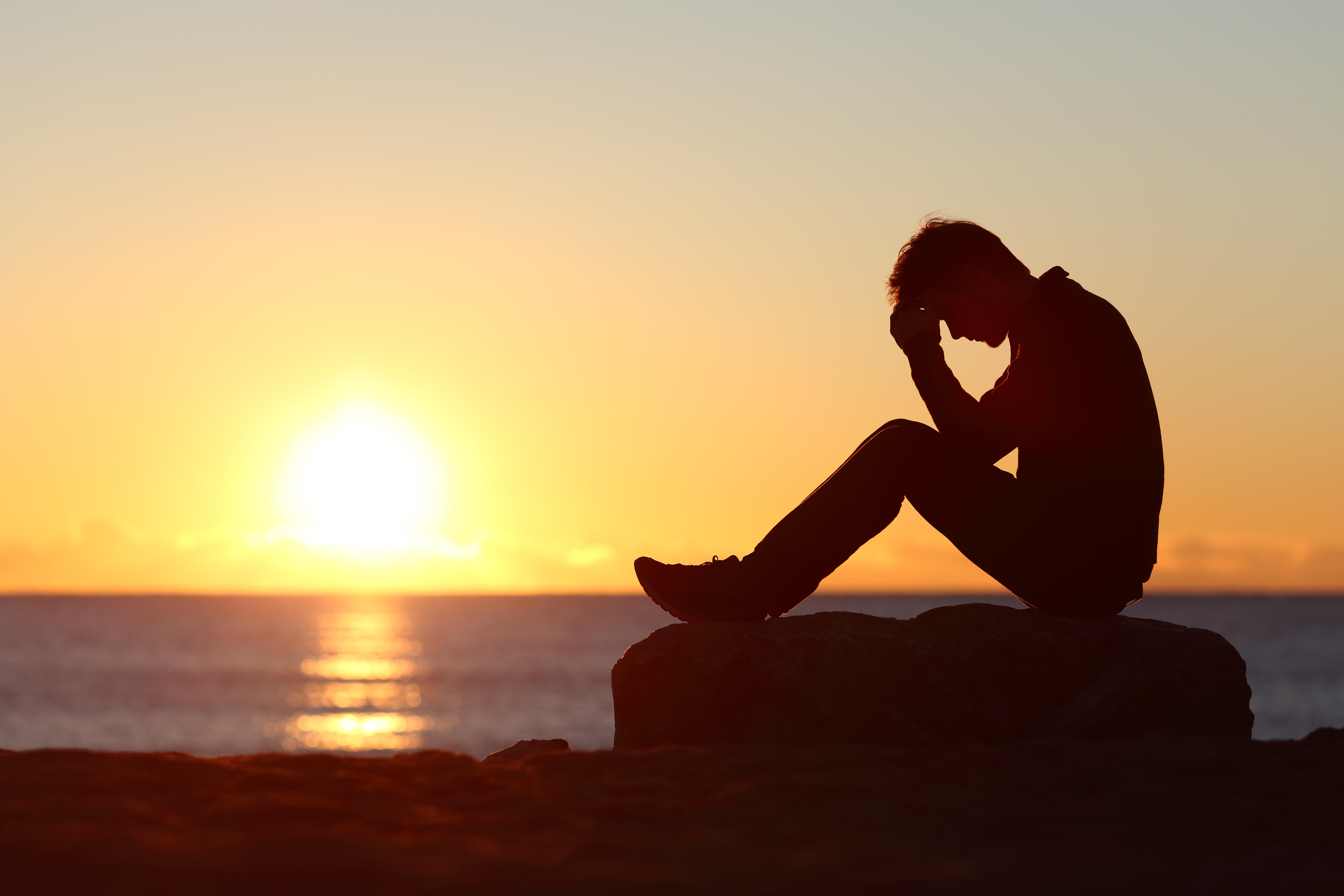 Man sitting worried on the beach at sunset with the sun in the background