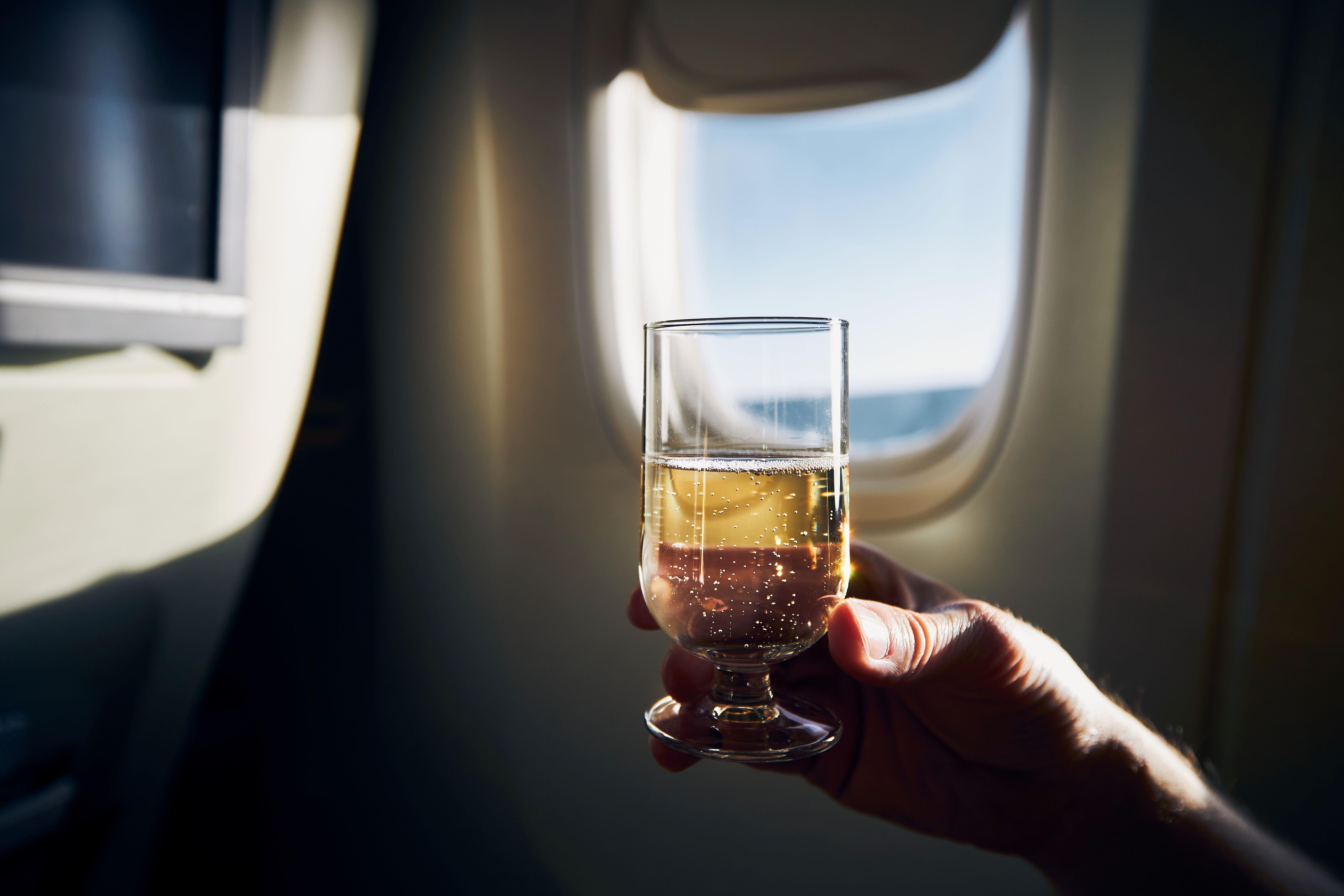 A man holding glass of sparkling wine against plane window (Alamy/PA)