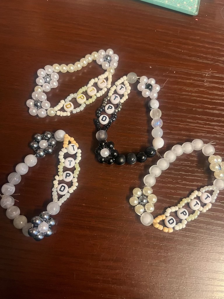 Four bracelets lying on a table with the letters 'TTPD' for Taylor Swift's album The Tortured Poets Department 