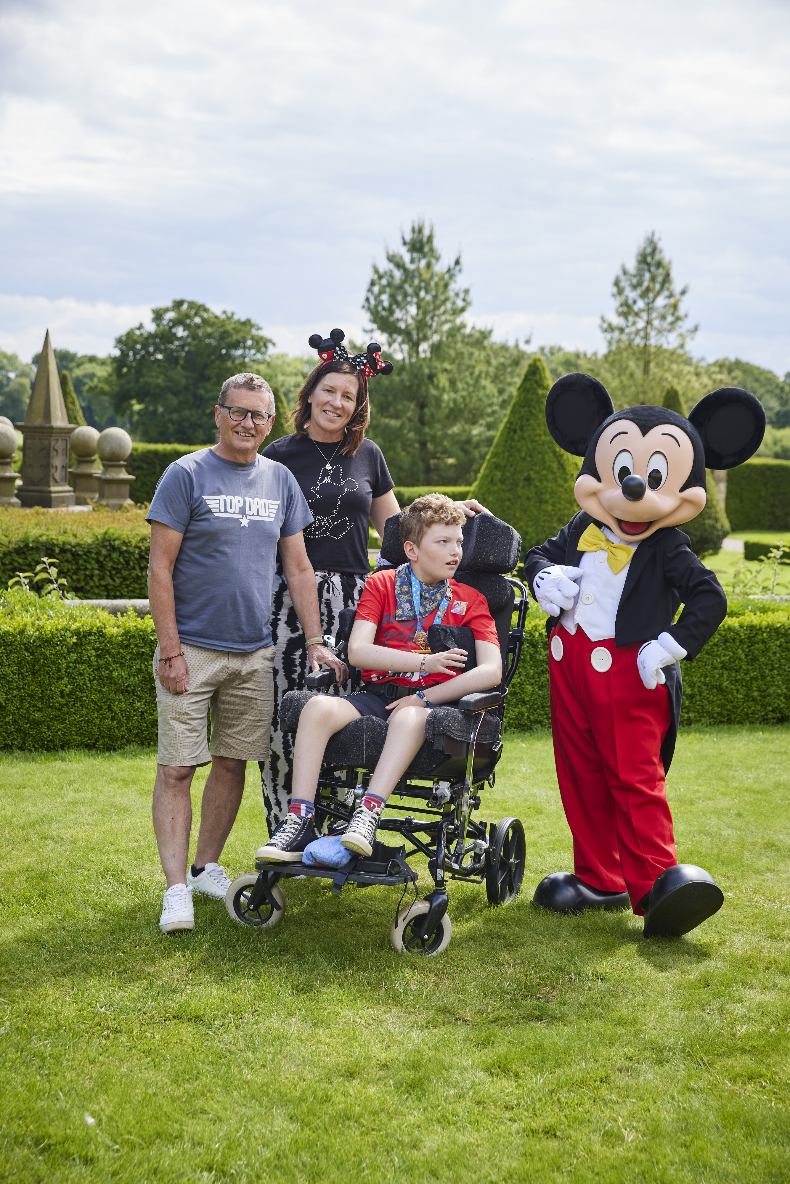Boy in wheelchair with parents and a man dressed as a mouse 