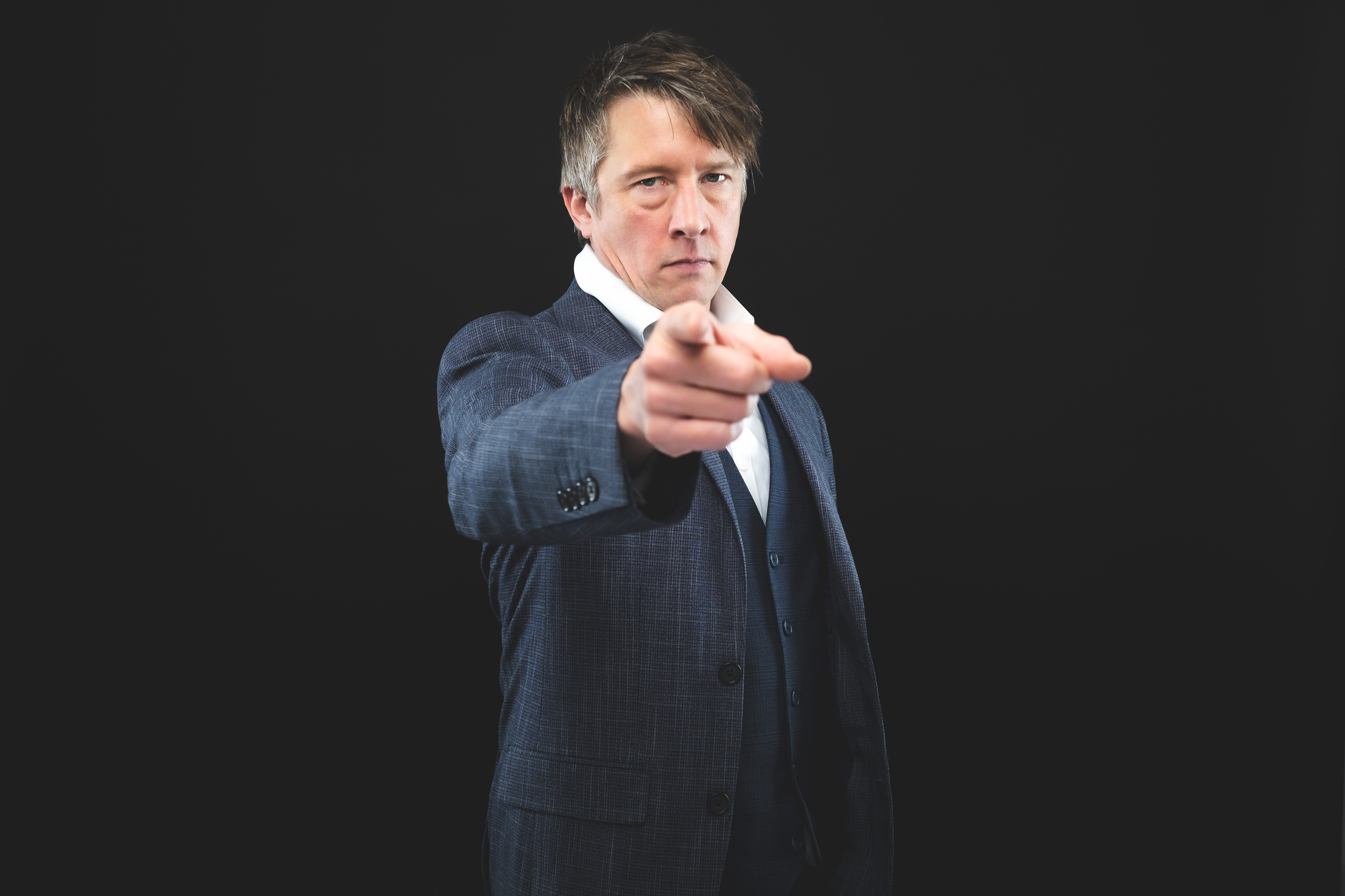 Jonathan Pie creator Tom Walker points and looks at the camera while standing in front of a black background