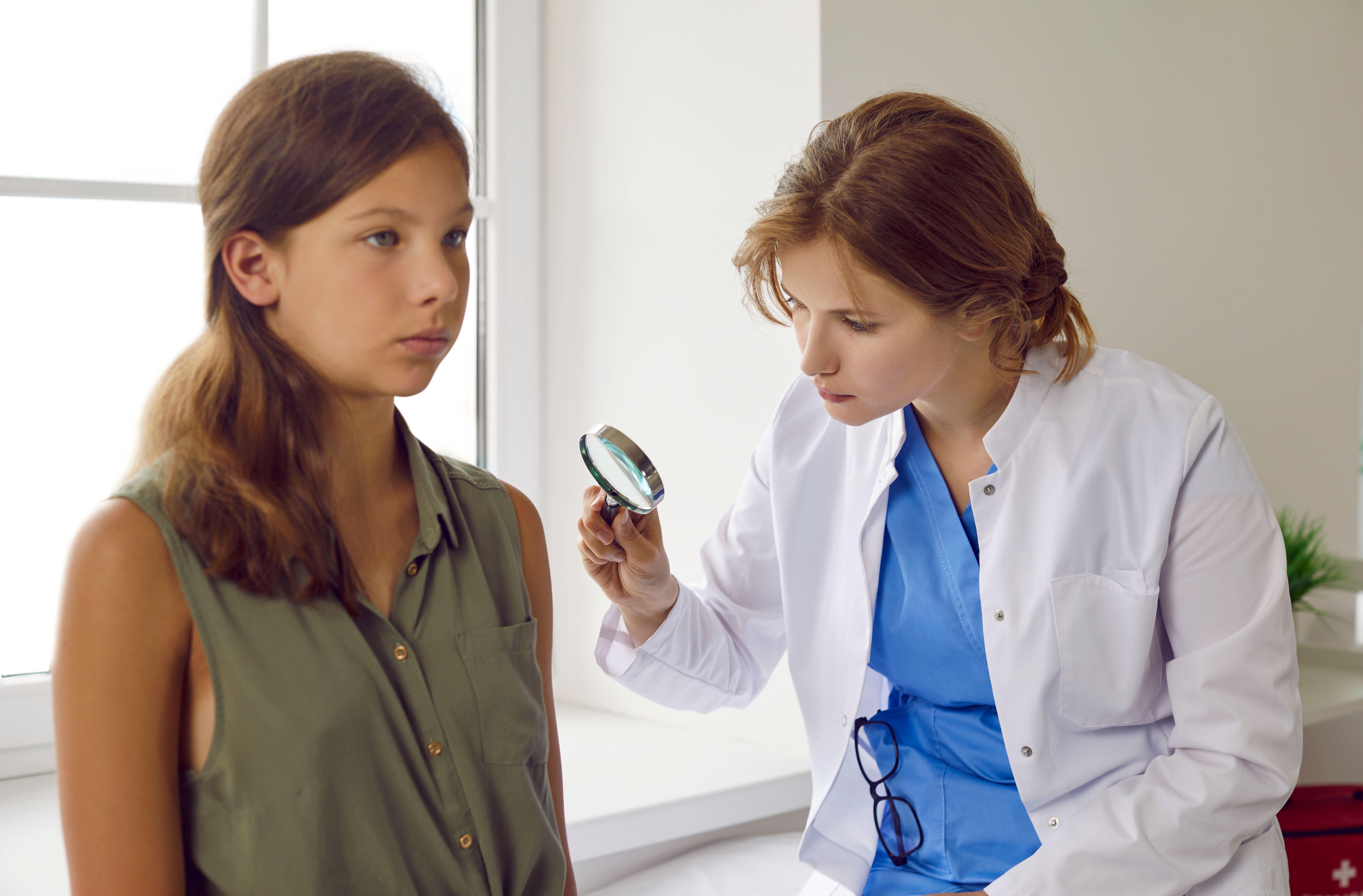 Dermatologist looking through magnifying glass while examining skin of child patient