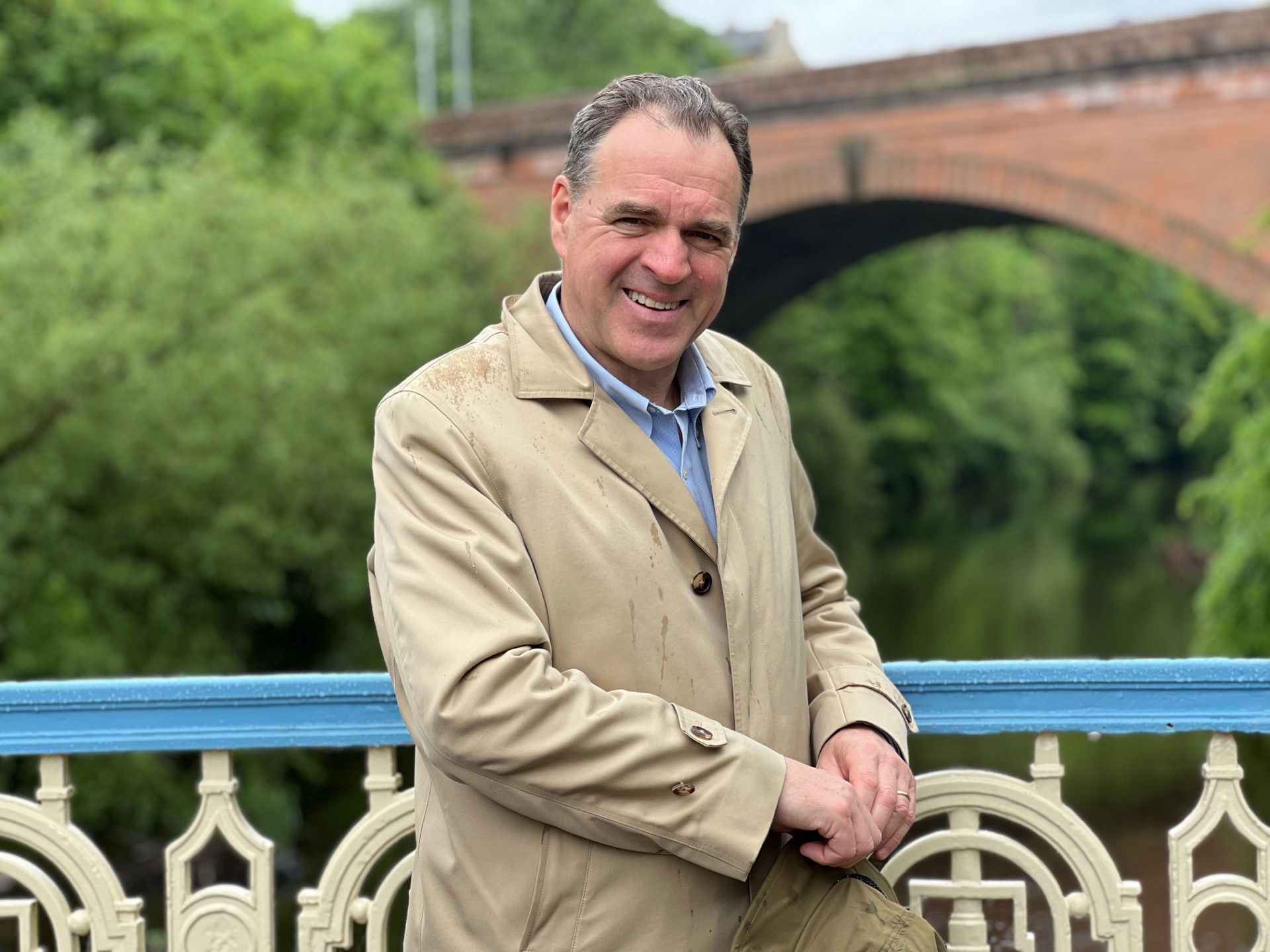 Professor Sir Niall Ferguson smiling, pictured with a bridge behind him