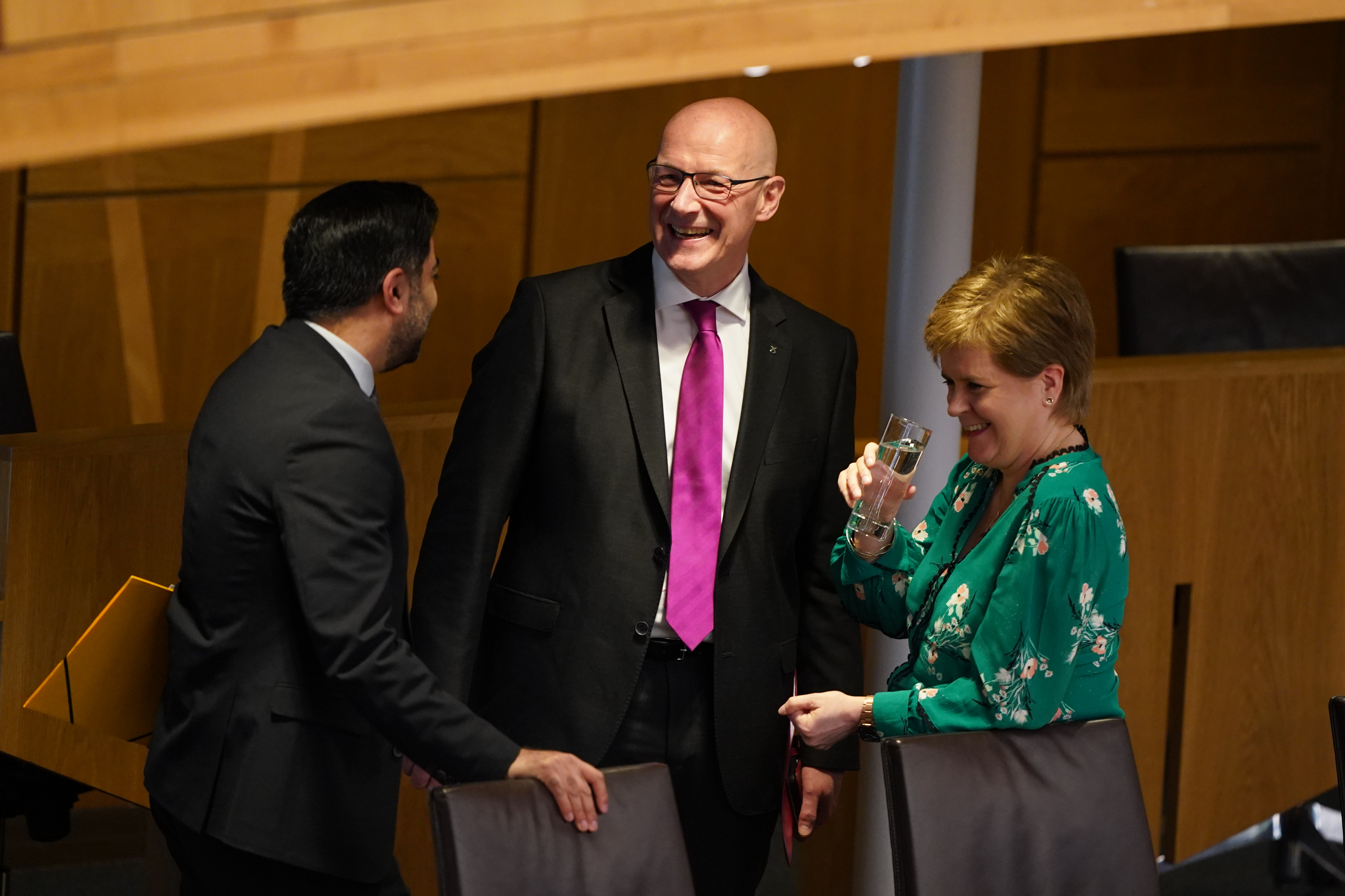 John Swinney smiles with Humza Yousaf to his left, and Nicola Sturgeon to his right