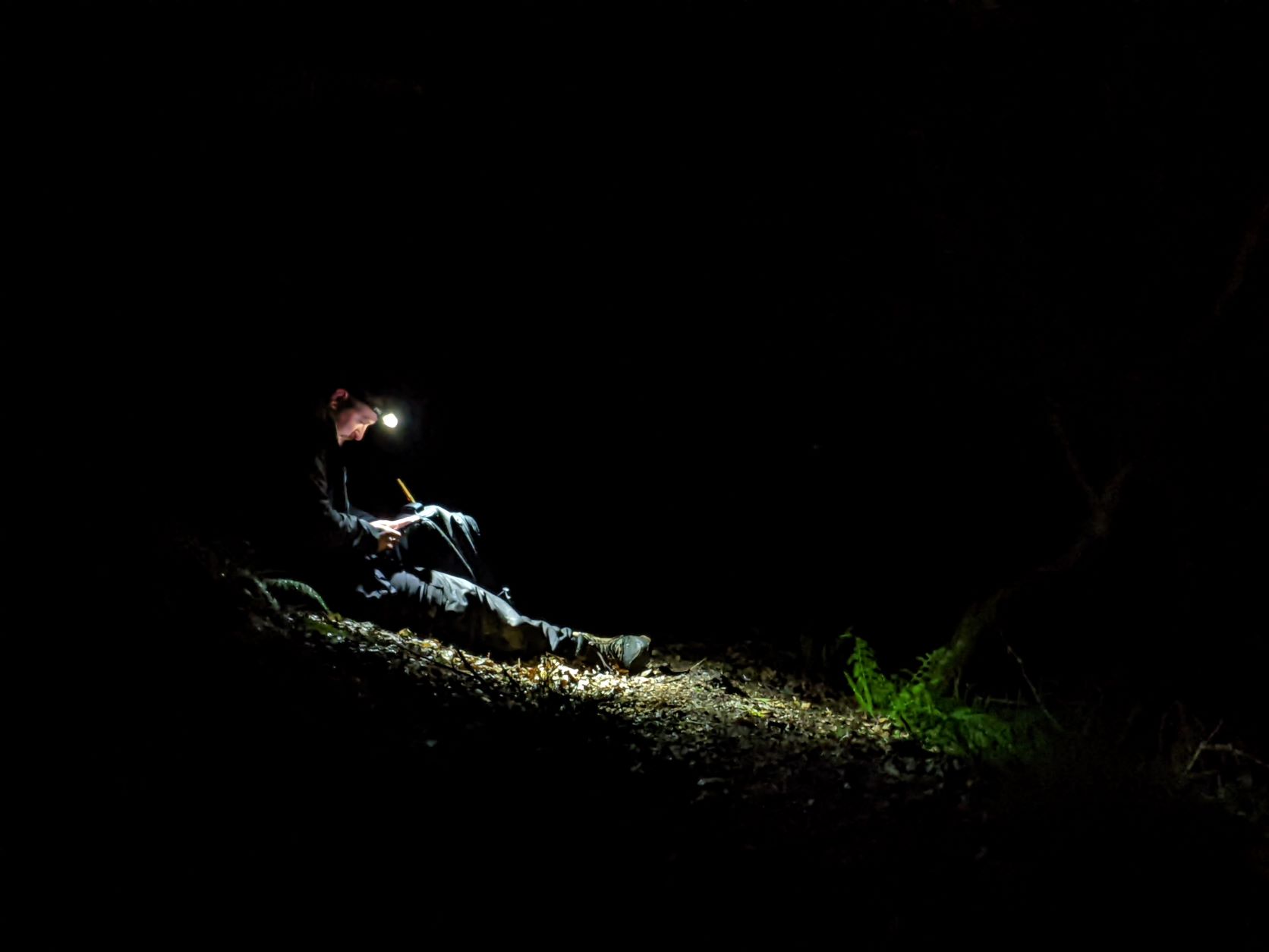 Brogan Pett wearing a head torch while sitting on the ground in the dark