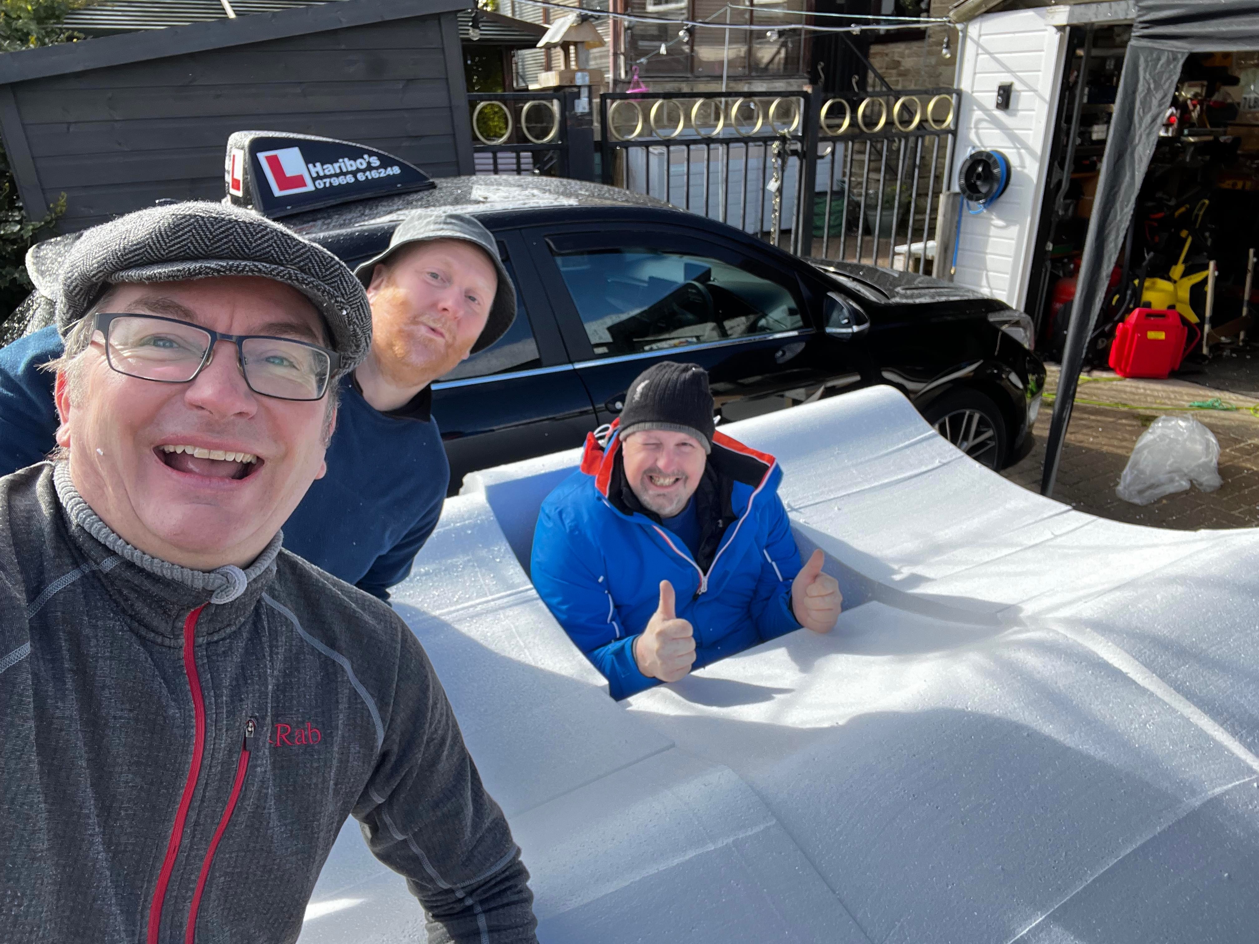 Three men smiling in a soapbox with a car in the background
