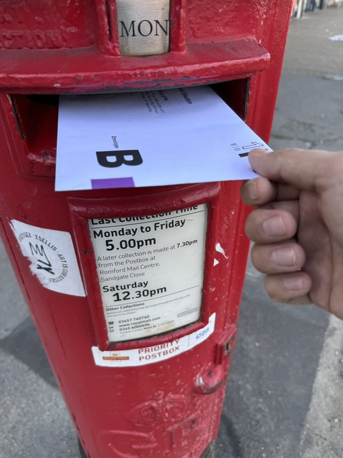 A envelope containing a postal vote being put into a red postbox