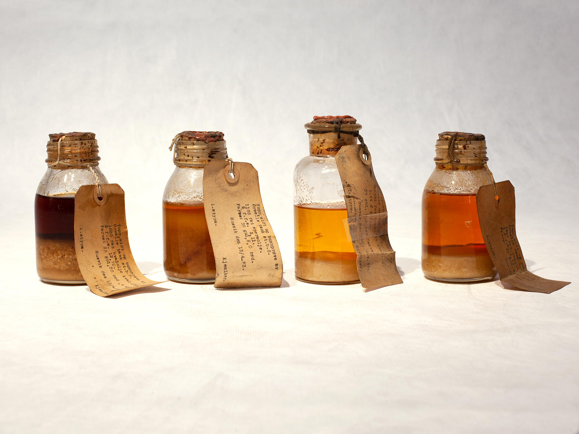 Four small bottles containing samples of whale oil with labels attached