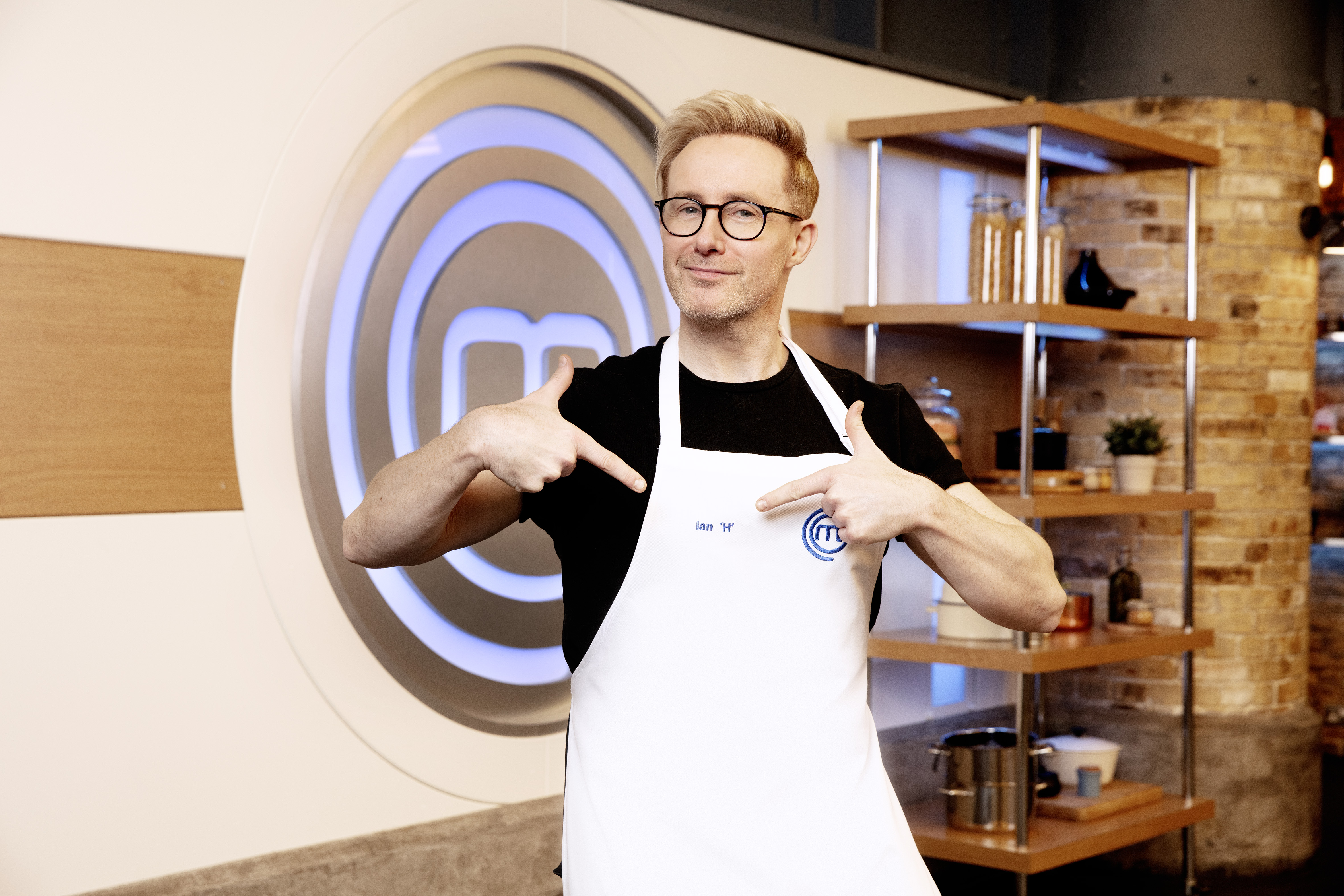 H from Steps points at his printed name of the MasterChef Celebrity apron