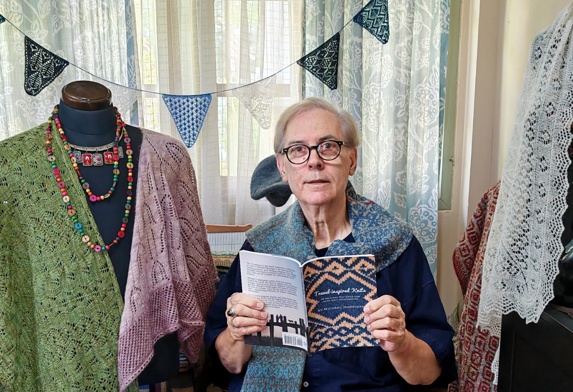Michael Harrigan surrounded by knitwear and holding a book