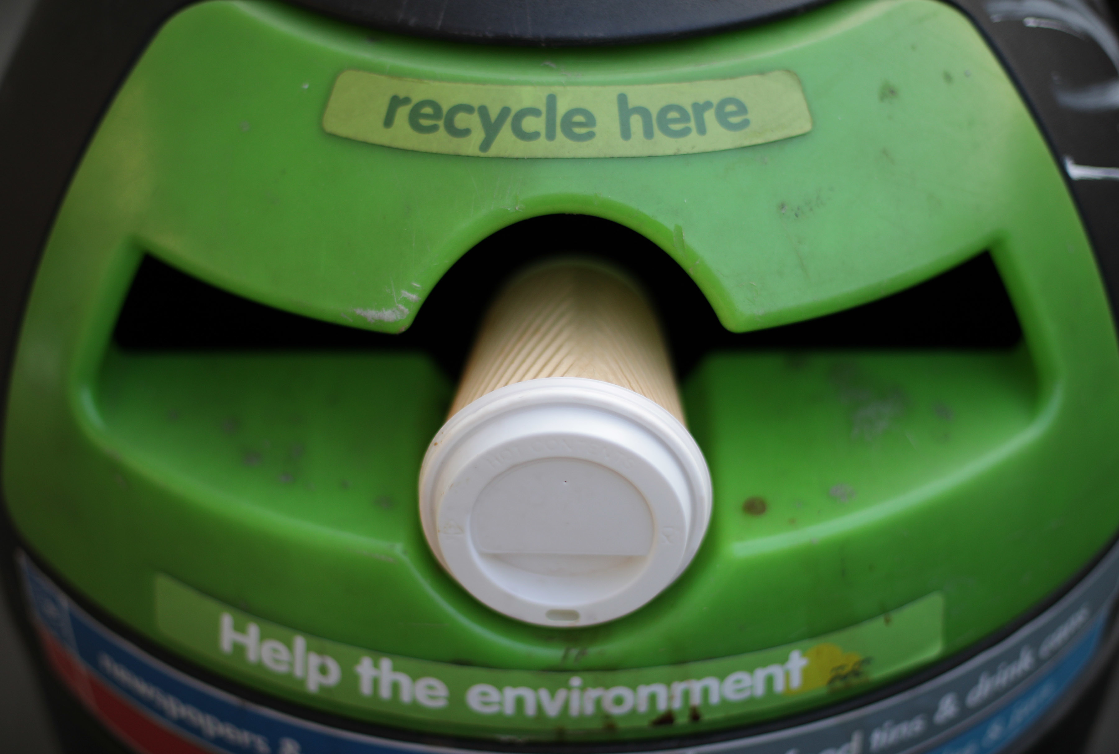 A coffee cup placed on a green recycling bin