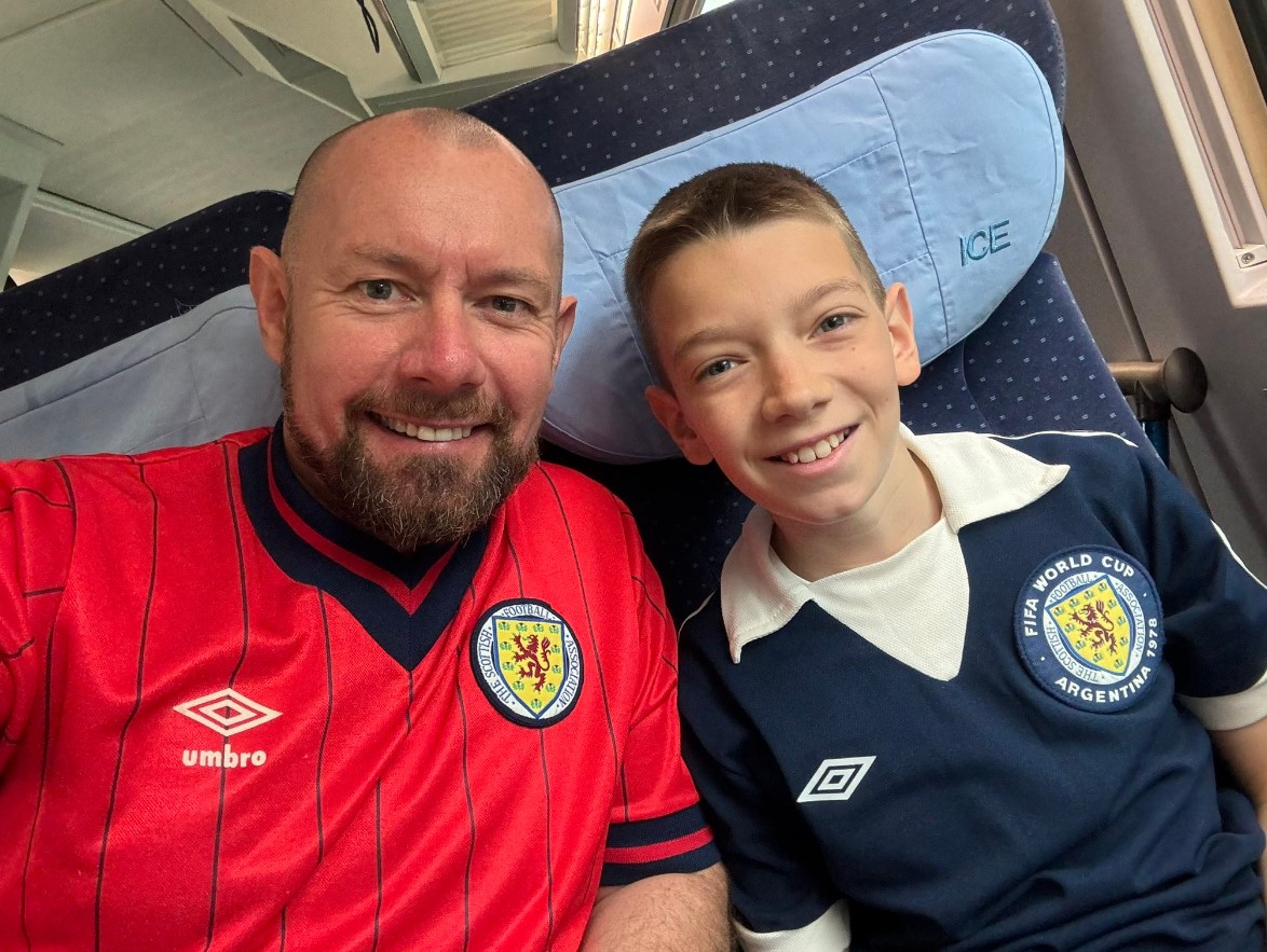 Iain and Aleks in Scotland shirts sitting on a train